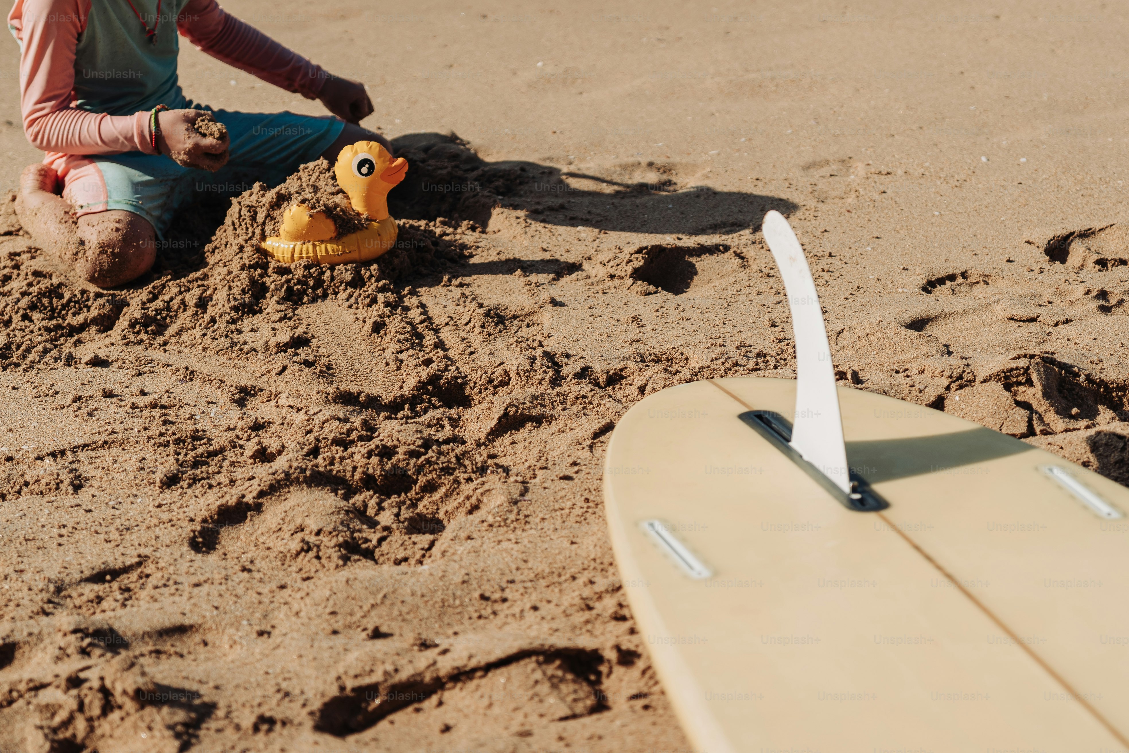 Kind, das am Strand mit Quietscheente und Surfbrett spielt