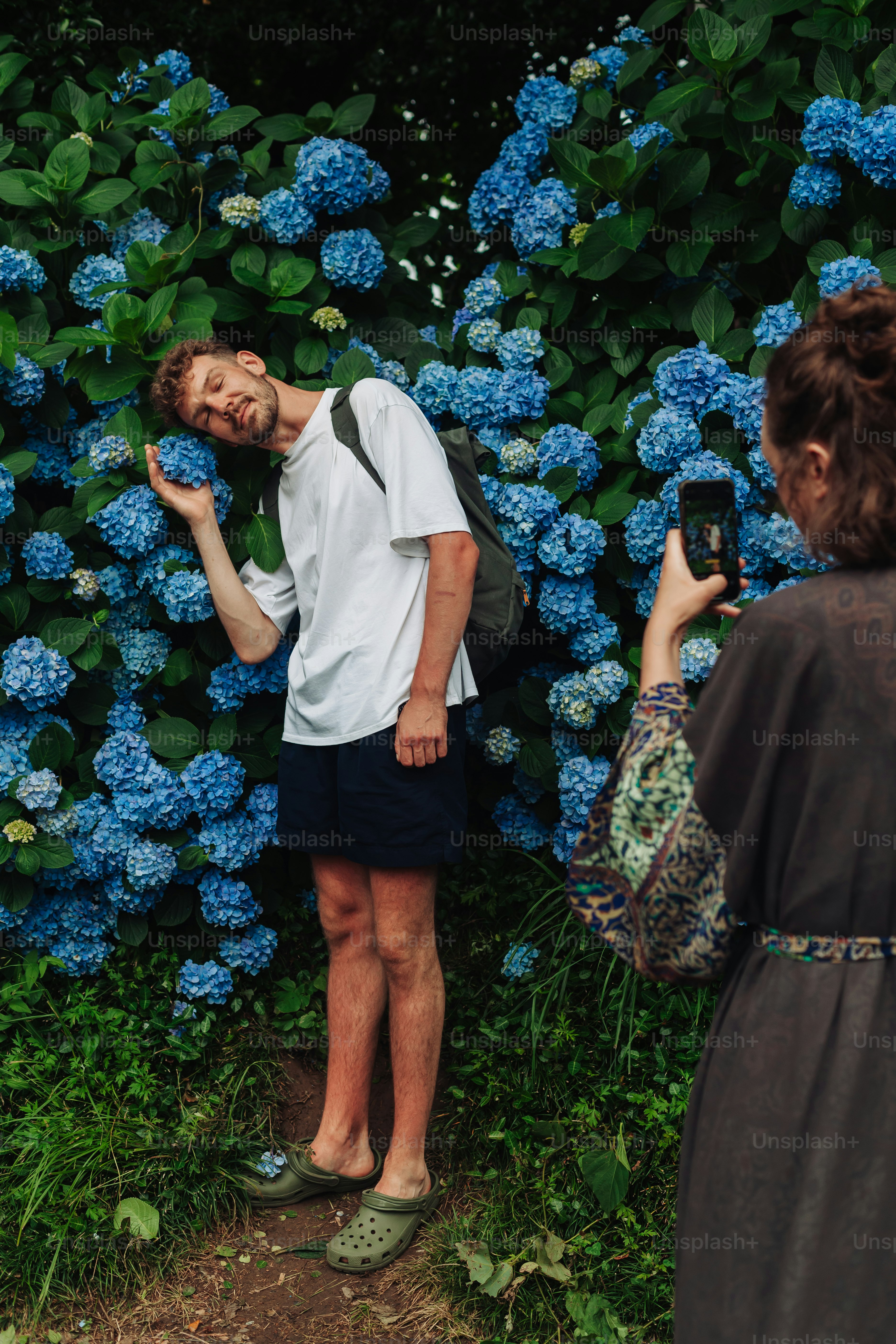 Frau fotografiert einen Mann, der mit blauen Hortensien posiert