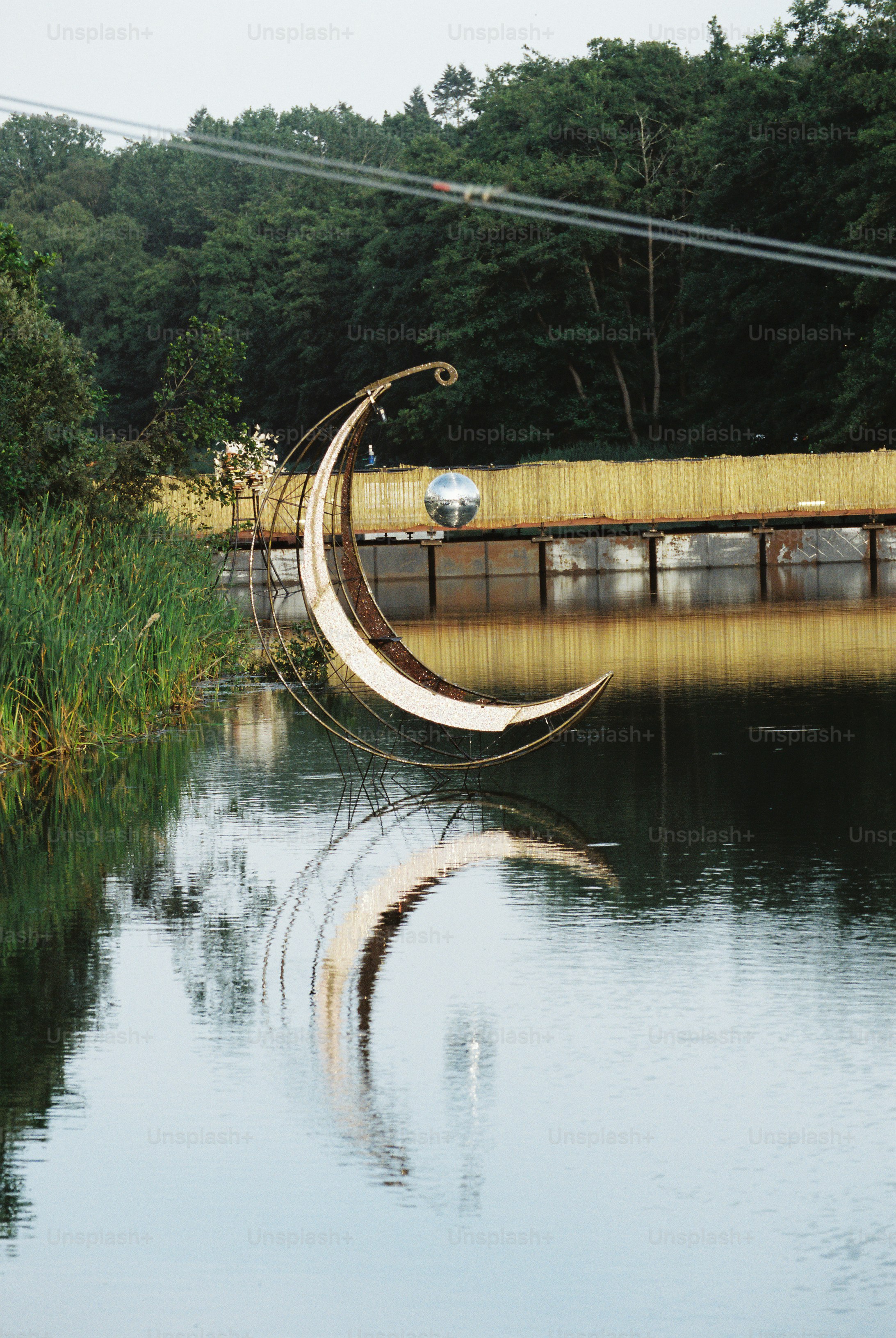 Sculpture de croissant de lune miroir se reflétant sur le lac, pont au toit de chaume.