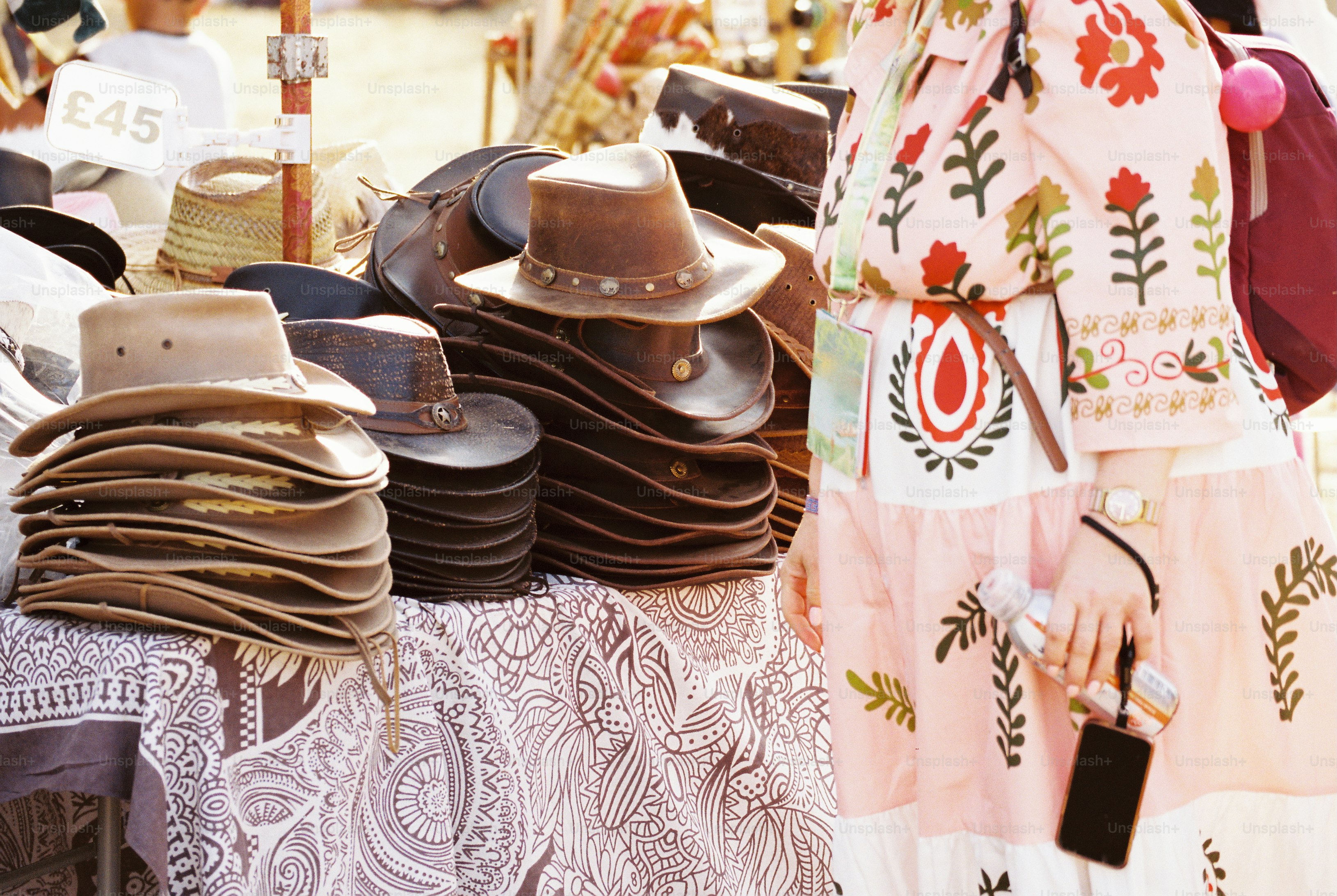 Femme en robe rose brodée à côté de chapeaux en cuir empilés