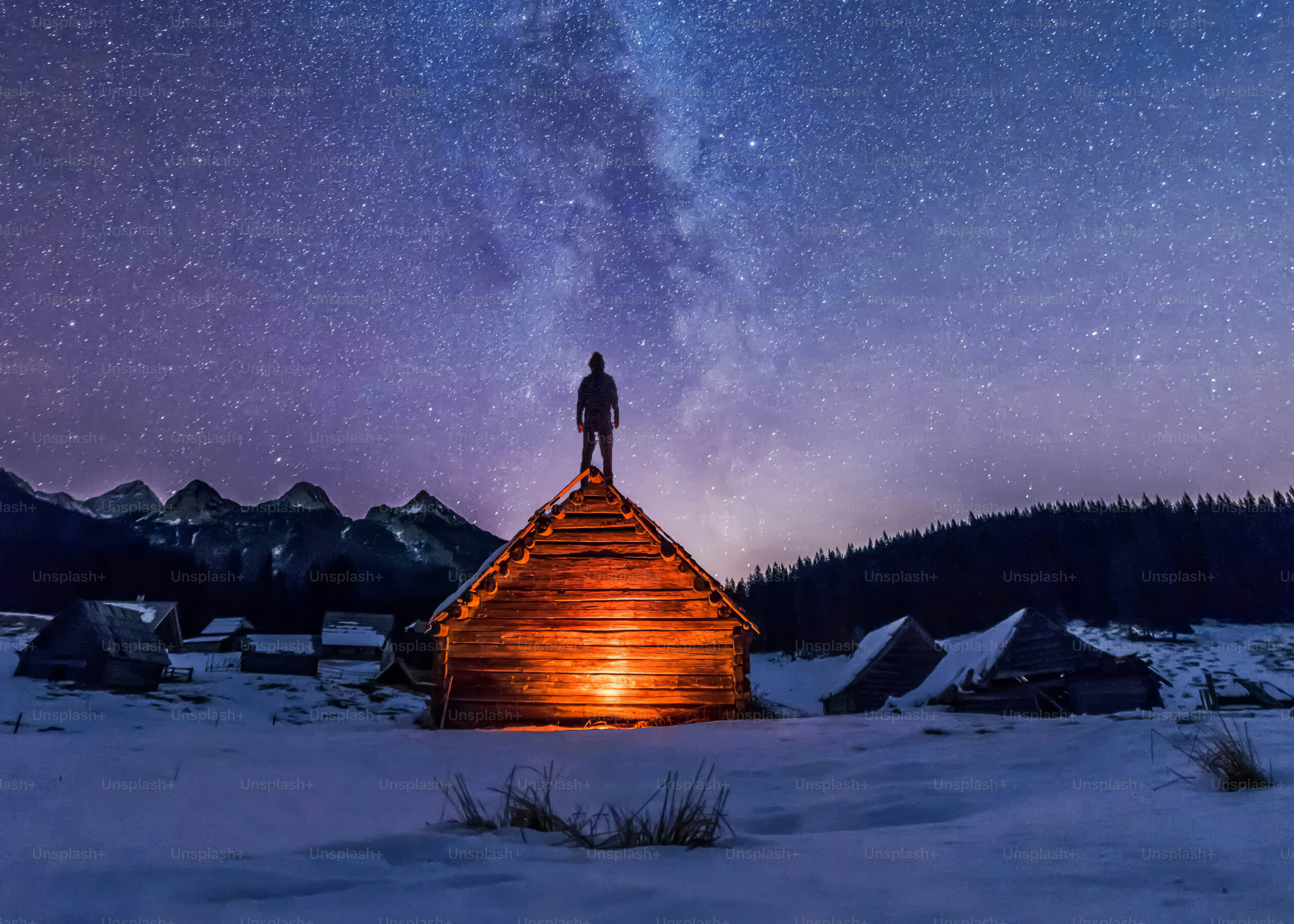 Man standing on glowing cabin roof under starry sky