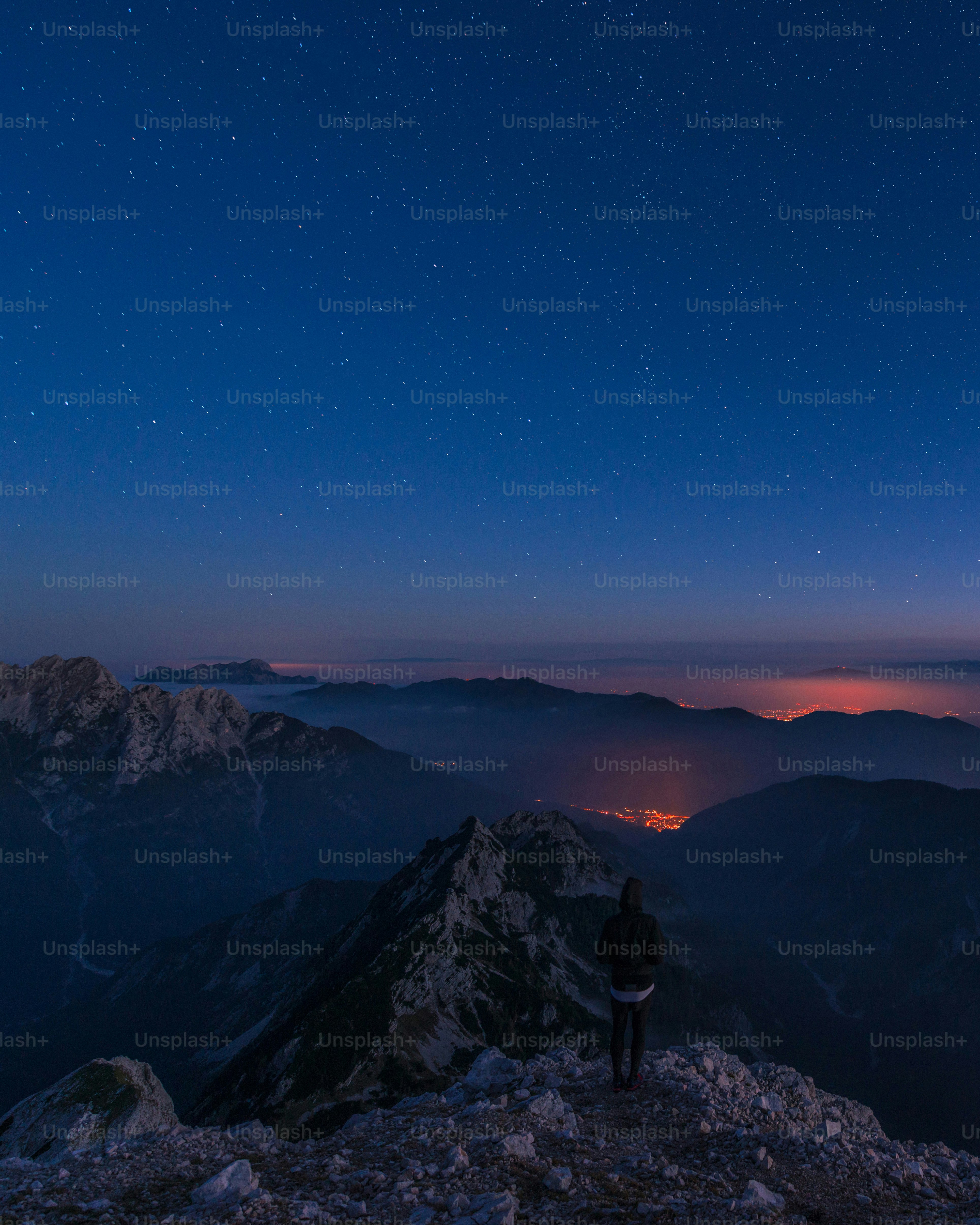 Person on mountain peak under starry sky, city lights