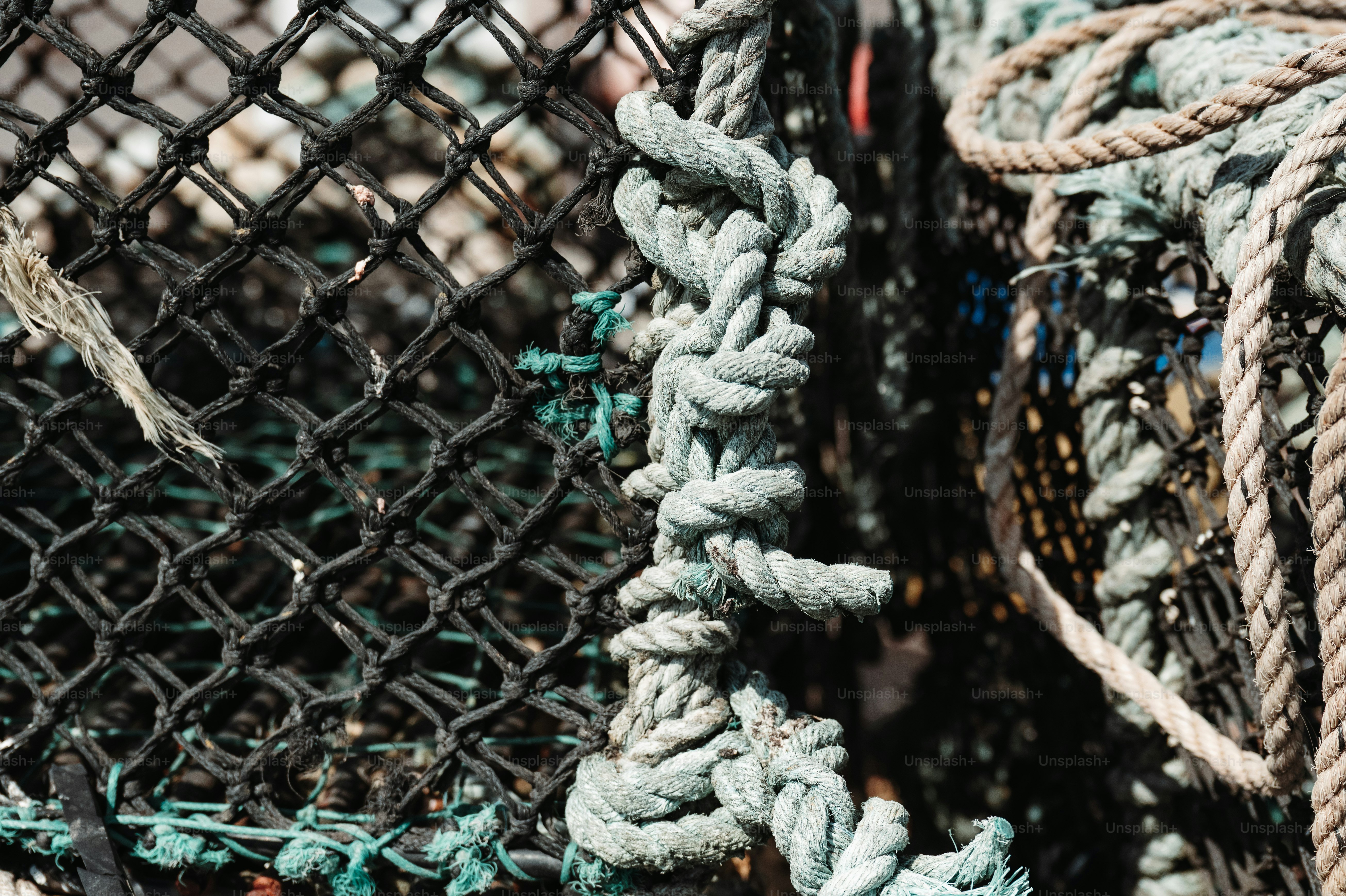 Une corde épaisse et grise nouée à un piège de pêche en maille noire.