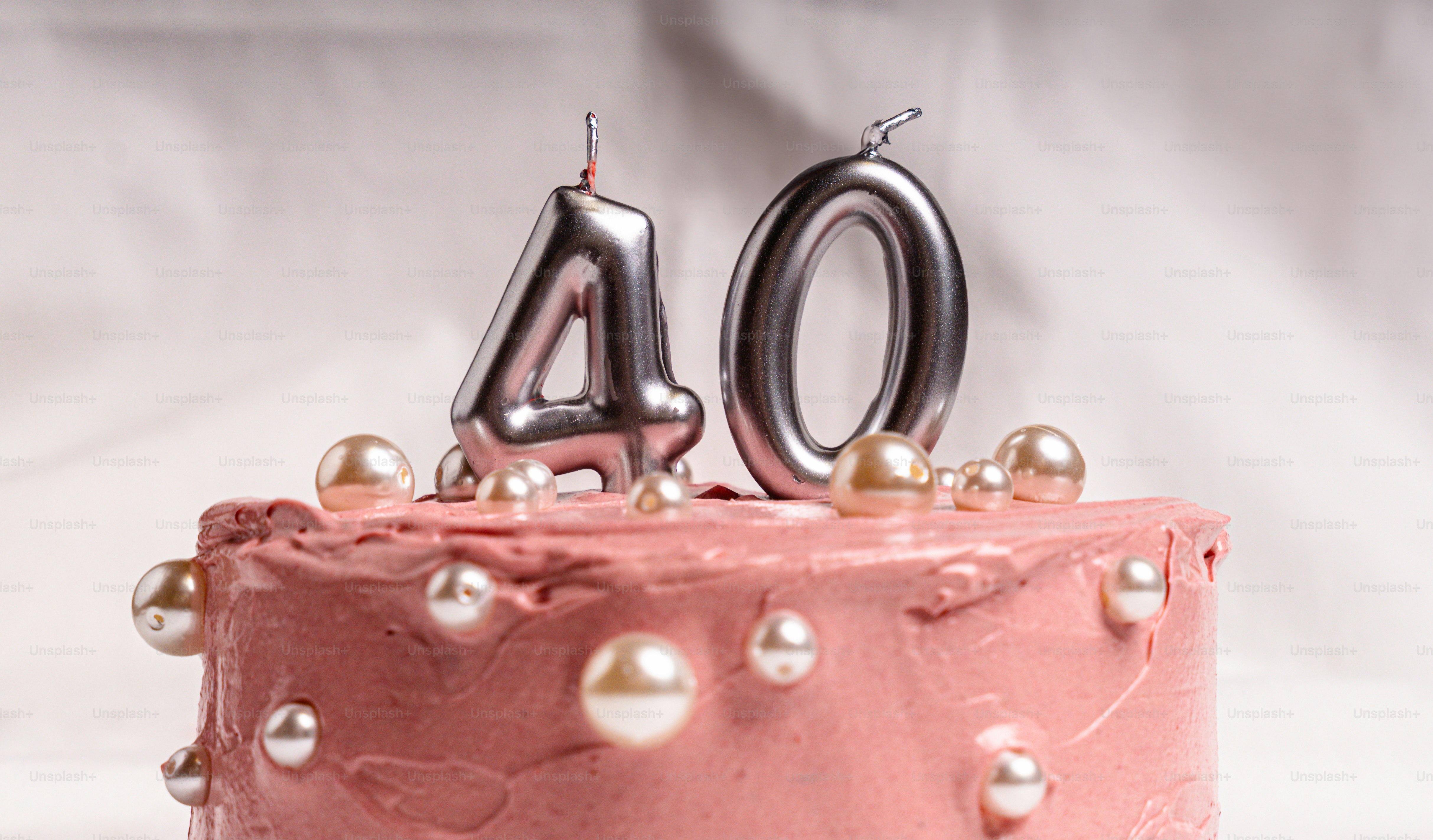 A pink frosted cake decorated with pearls and silver number forty candles