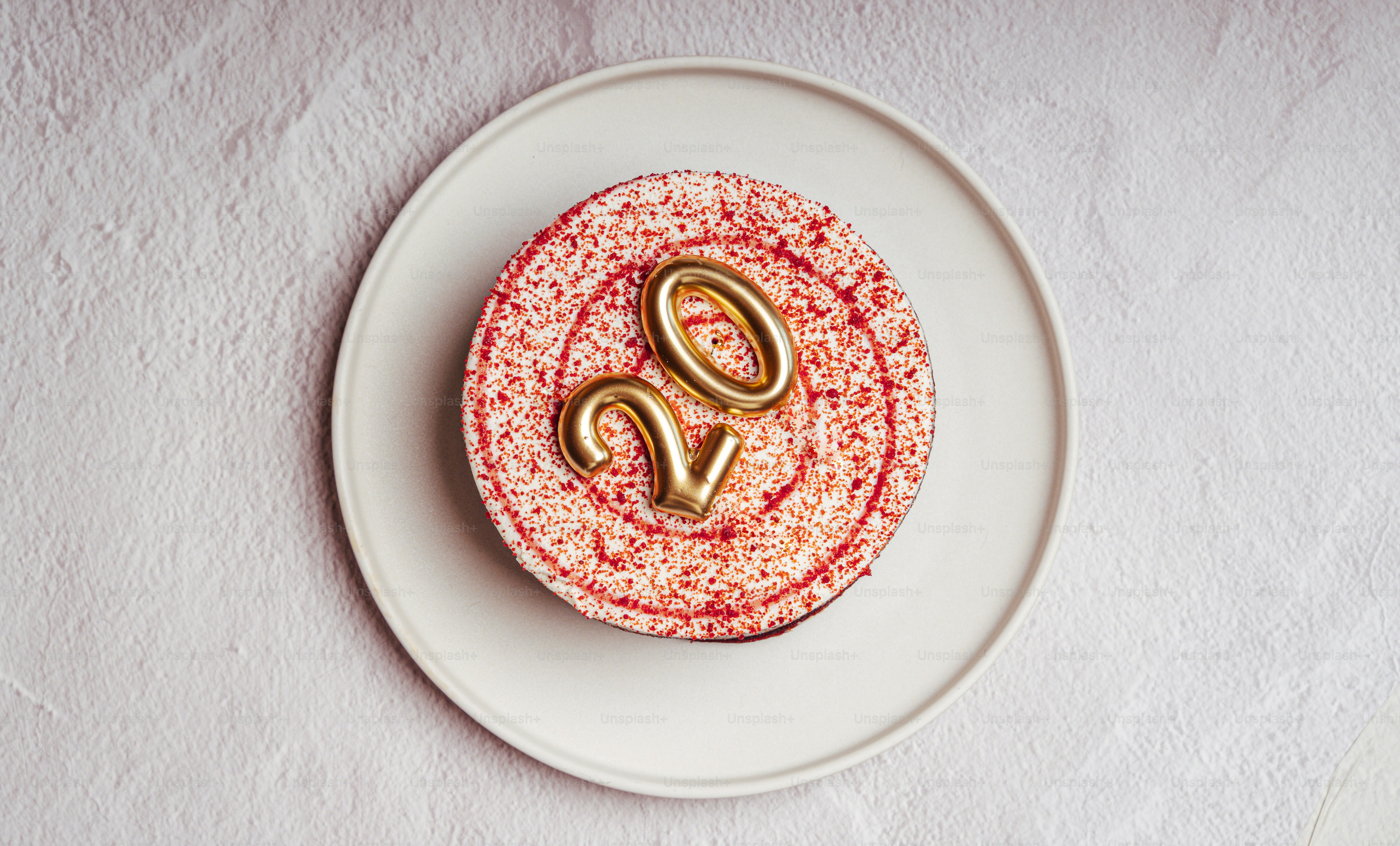 Pink frosted cake with golden 20 on white plate