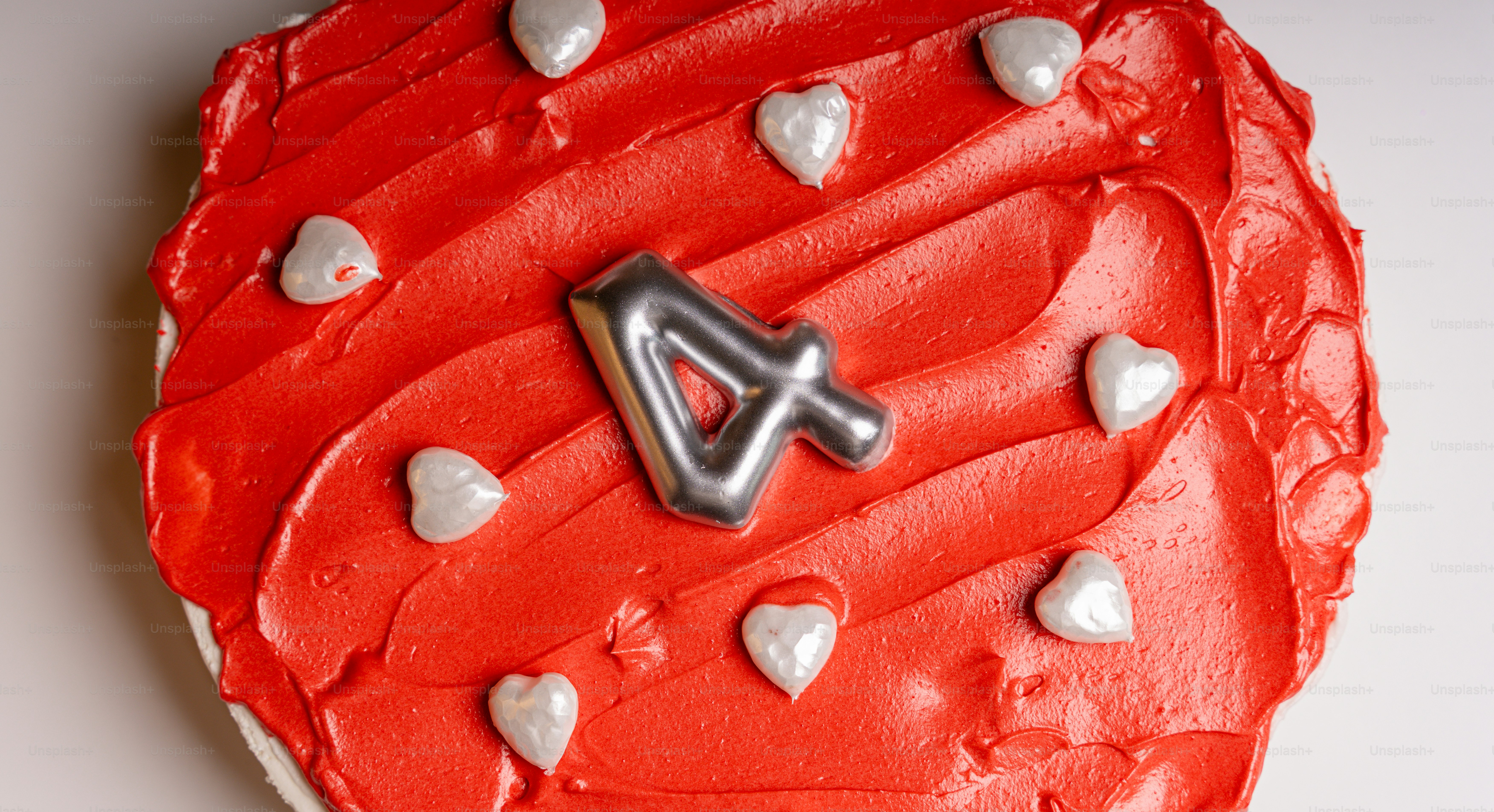 A cake with red frosting, white heart decorations, and a silver number four candle