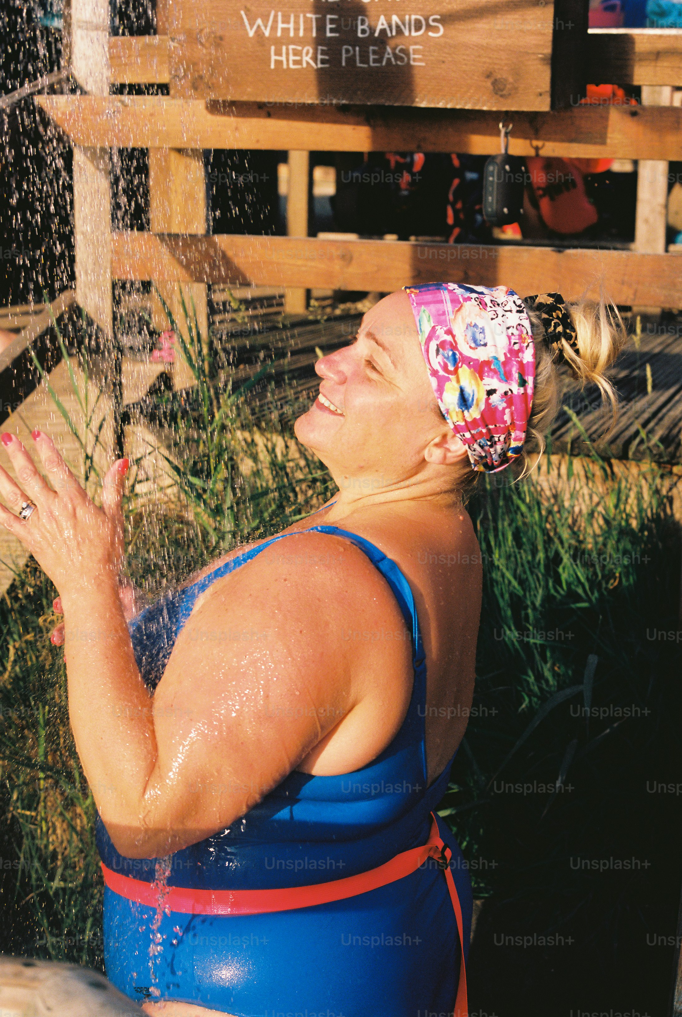 Smiling woman in blue swimsuit under an outdoor shower