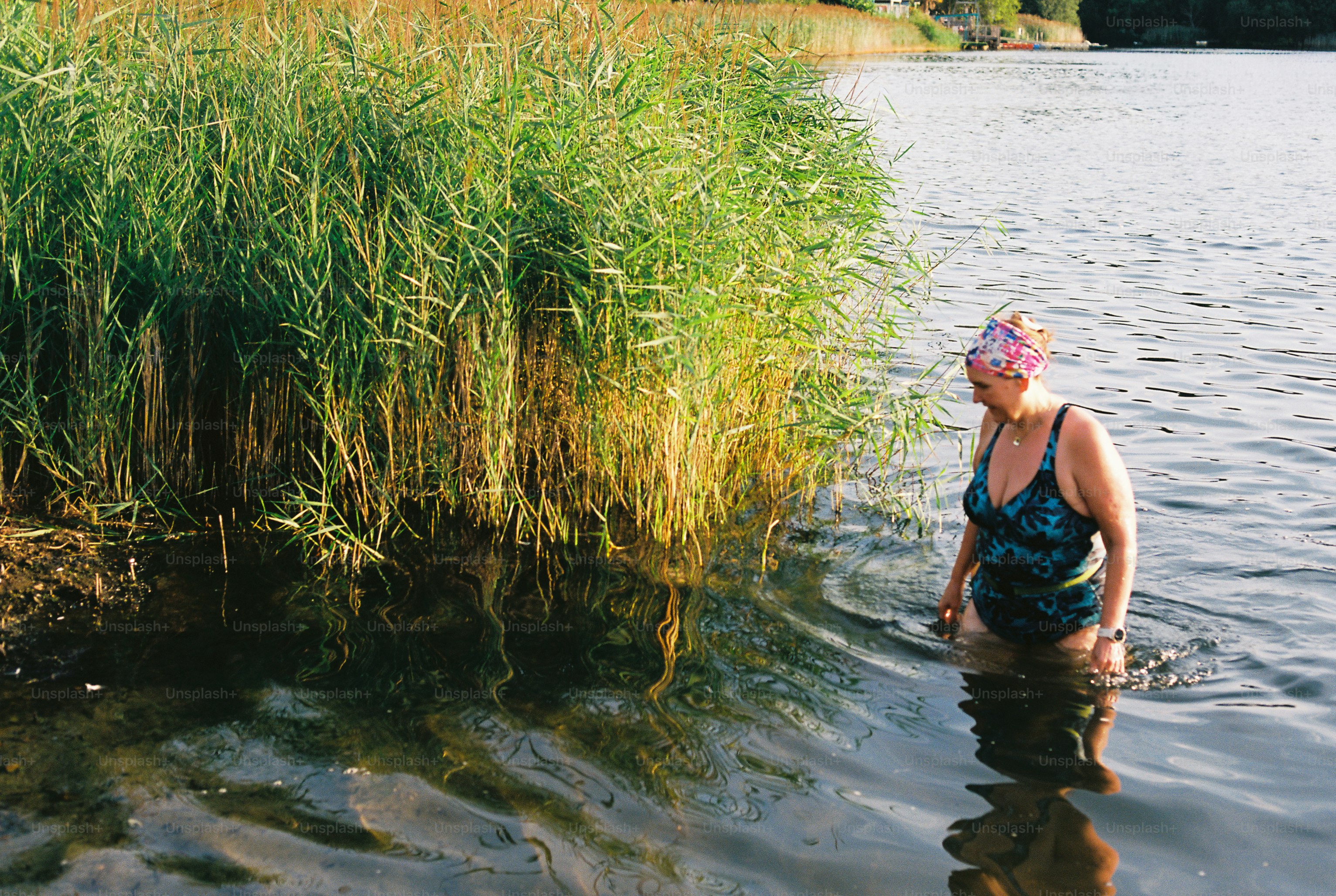 Woman in swim cap entering water beside tall reeds