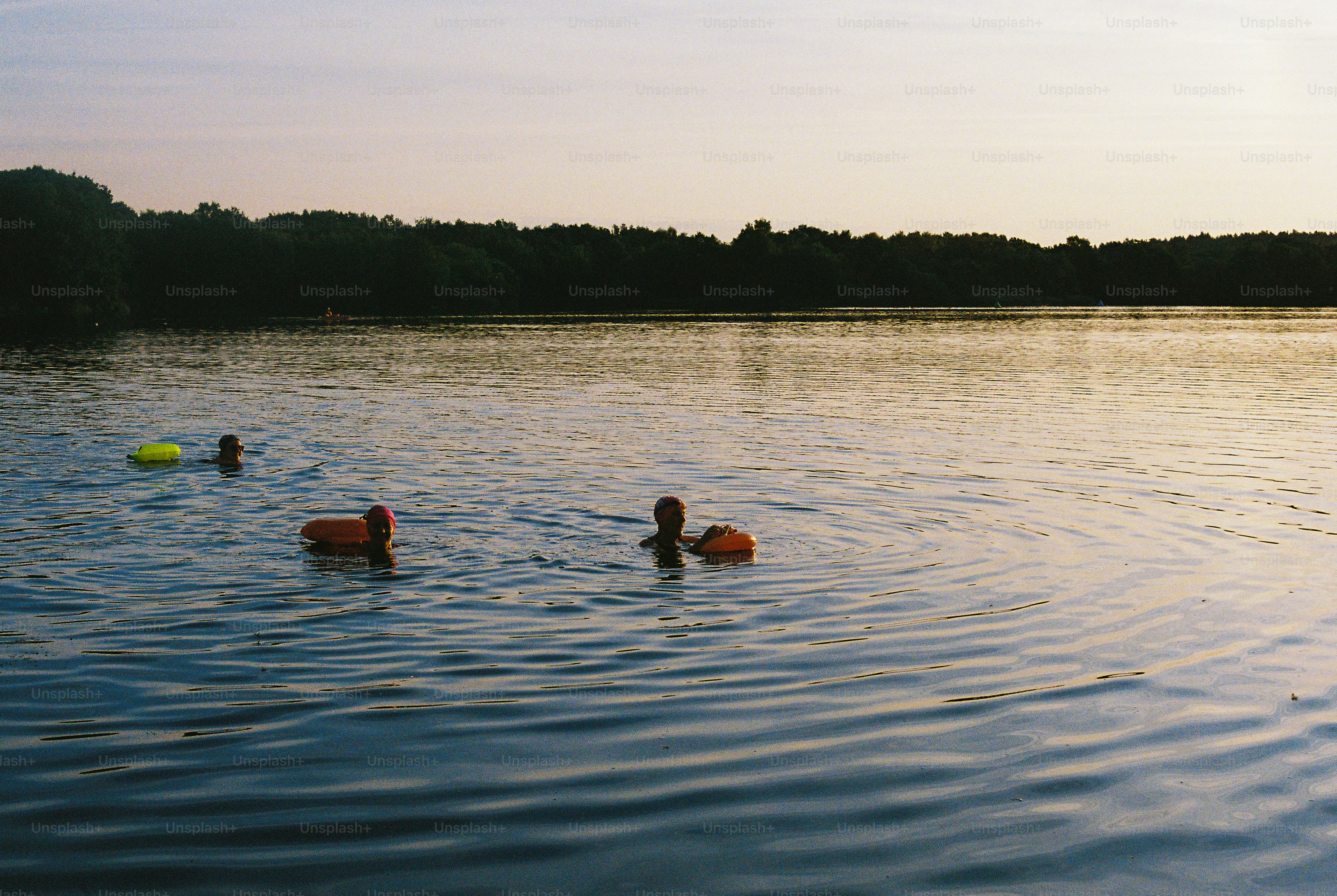 Swimmers in lake with flotation devices at dusk