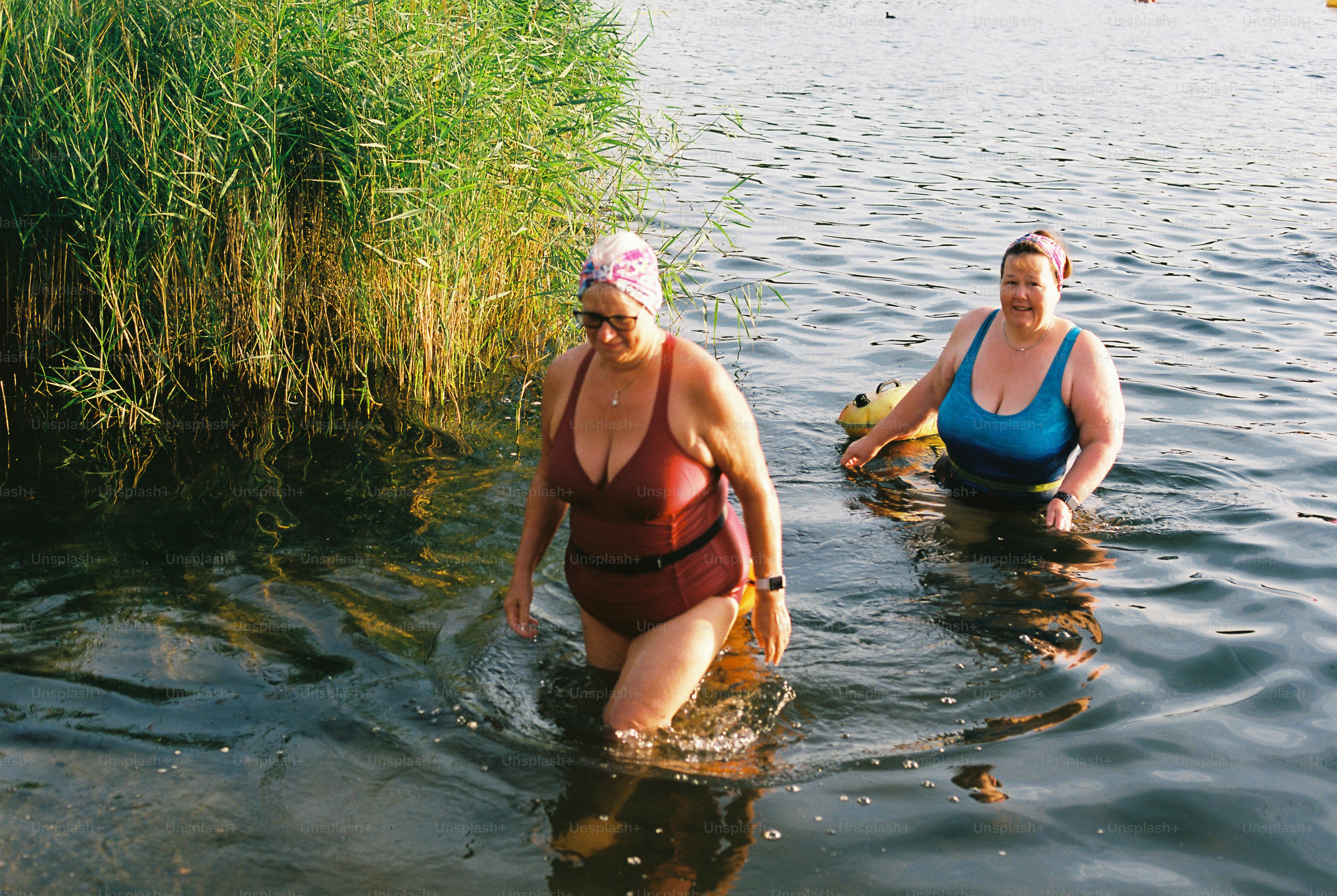 Two women wading in water with reeds