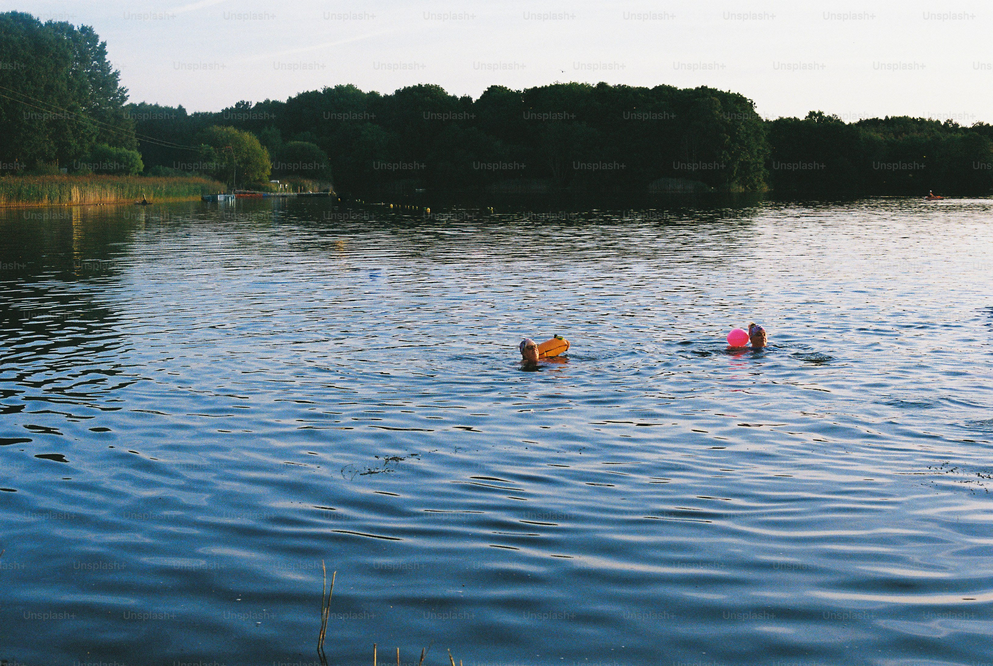 People swimming in a lake carrying colorful floats