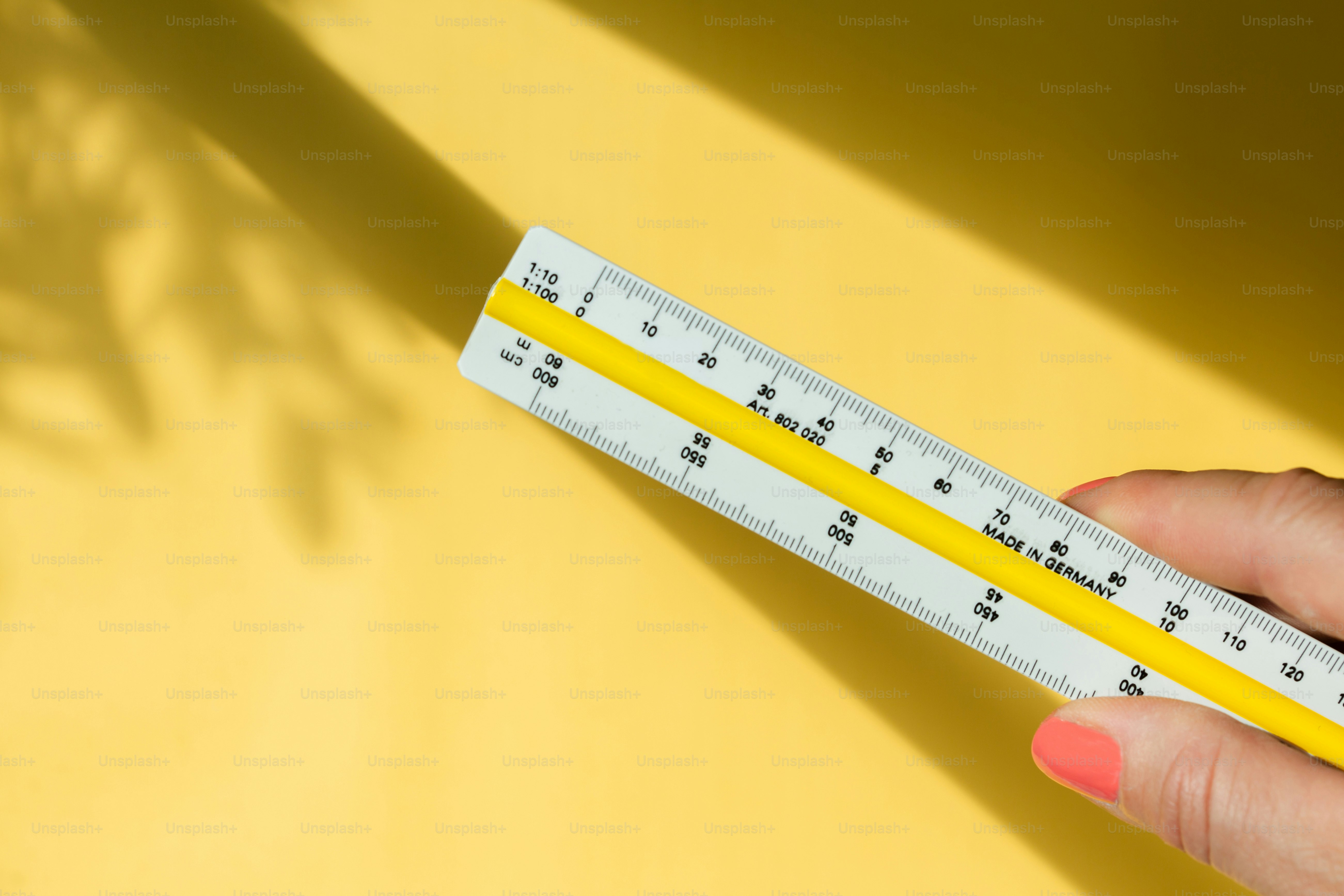 Hand holding white ruler on yellow background with leaf shadows