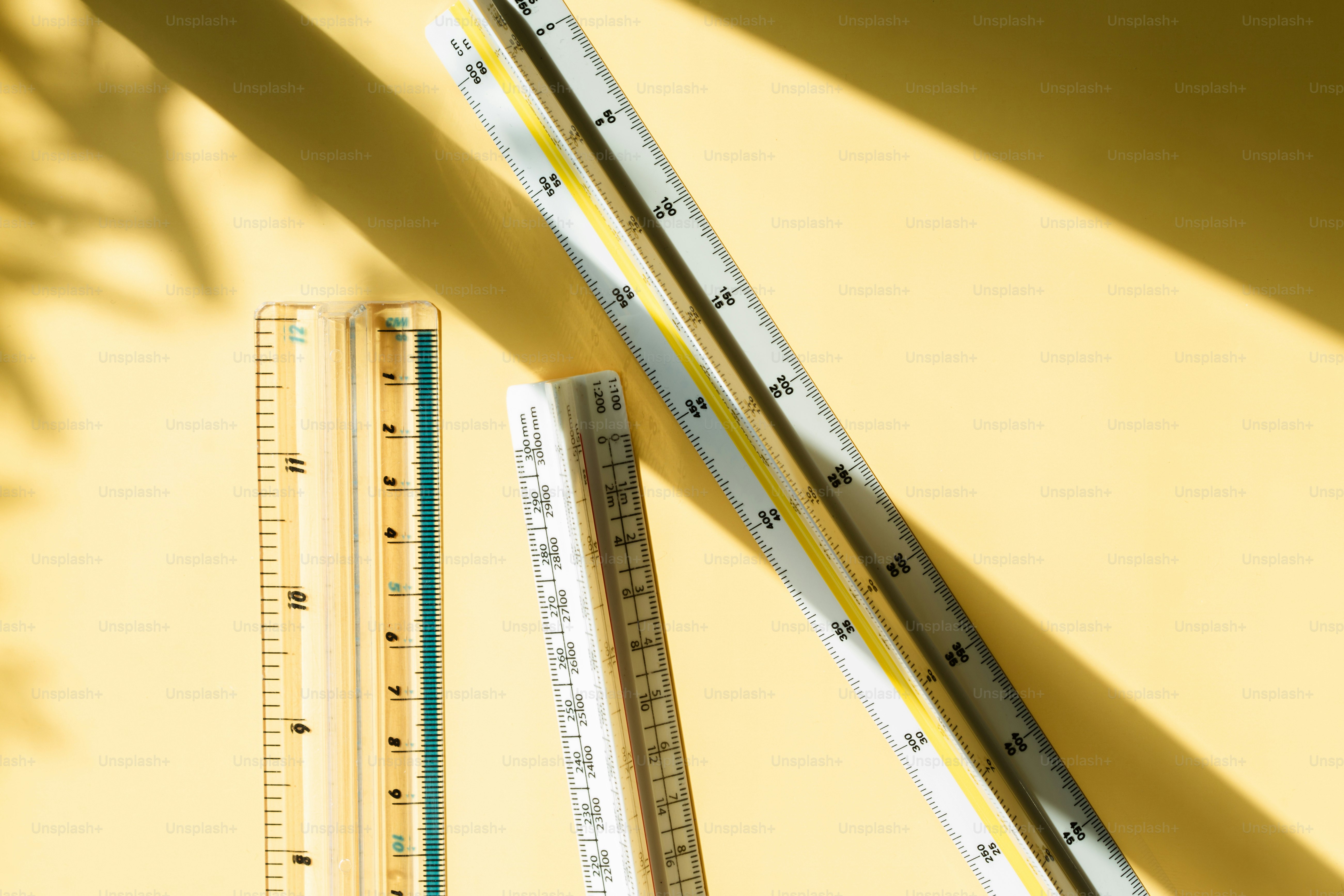Architectural rulers on yellow surface with dappled shadows