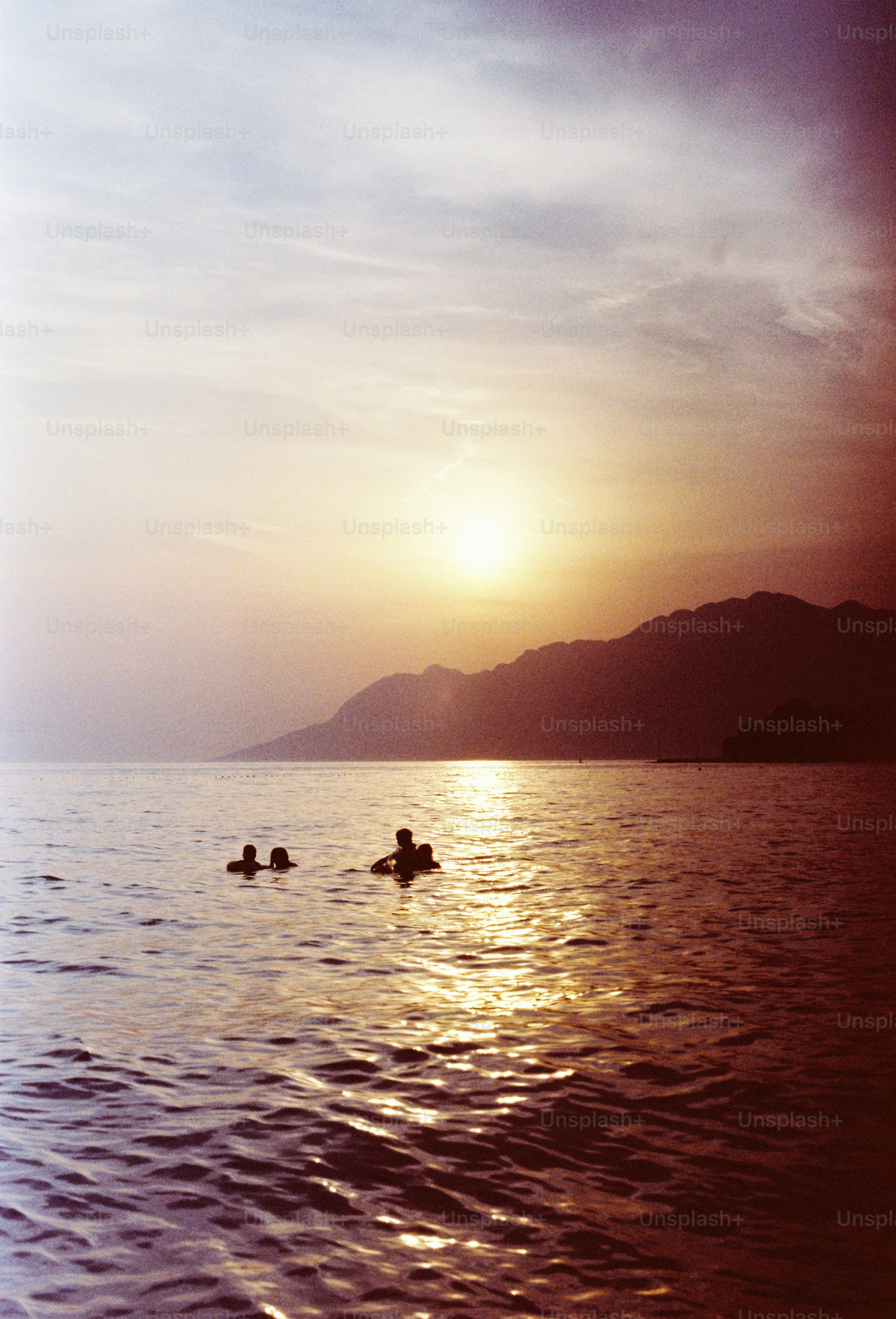Sunset over ocean with swimmers and mountains
