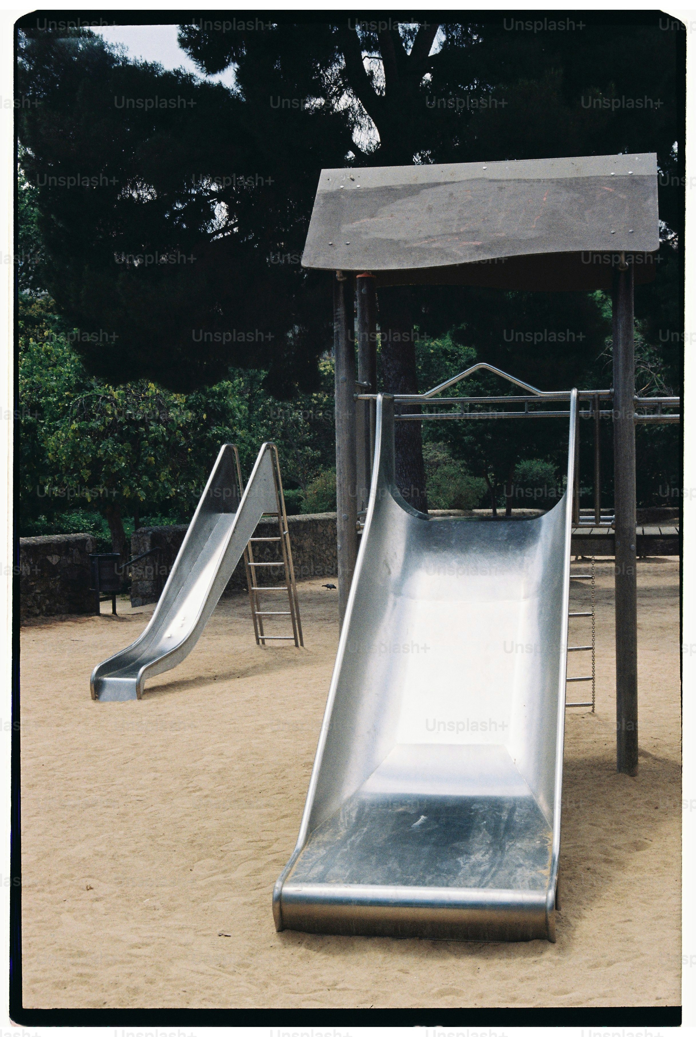 Two metal slides in a sandy playground