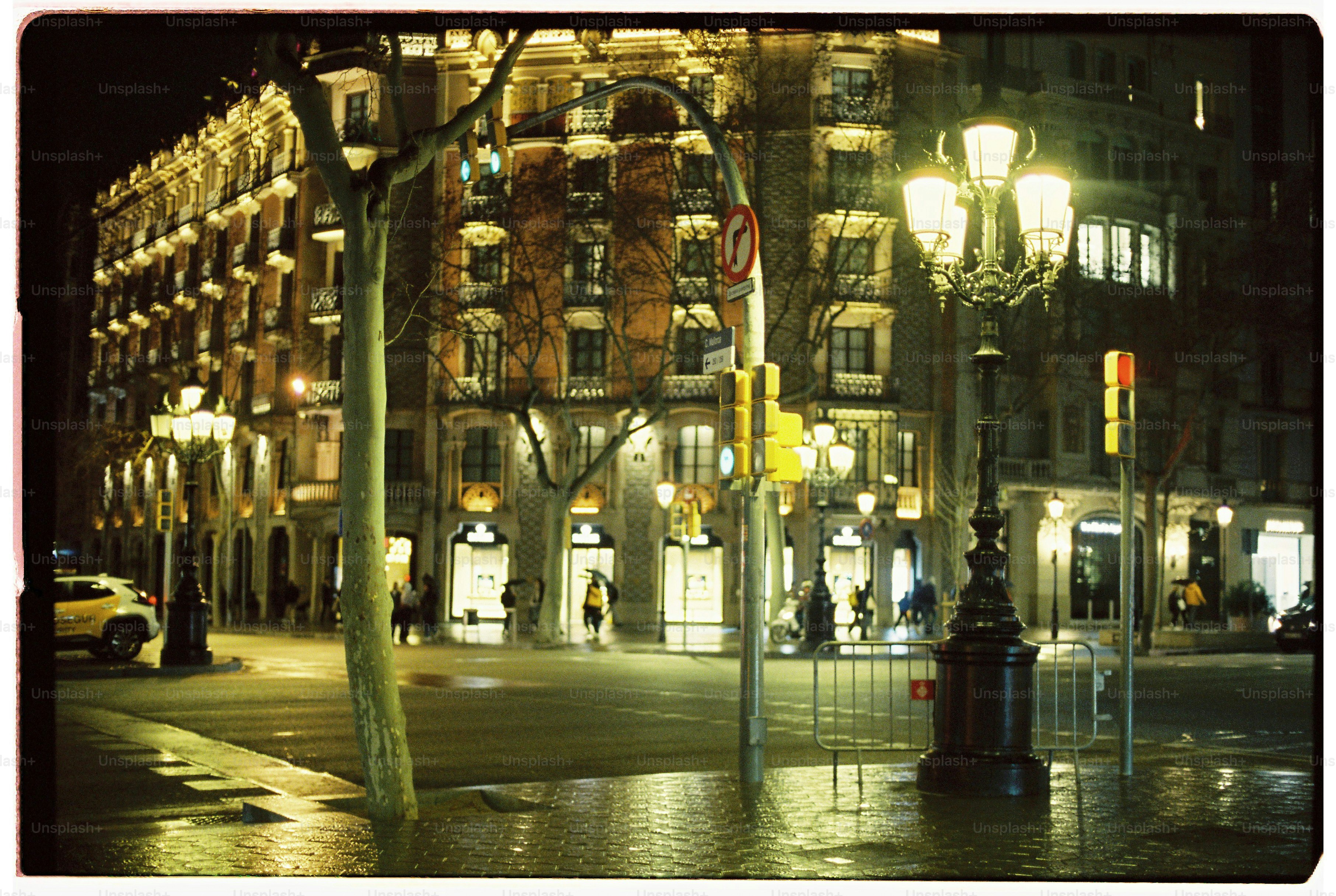 A street corner at night with ornate lamp posts and illuminated building facades.