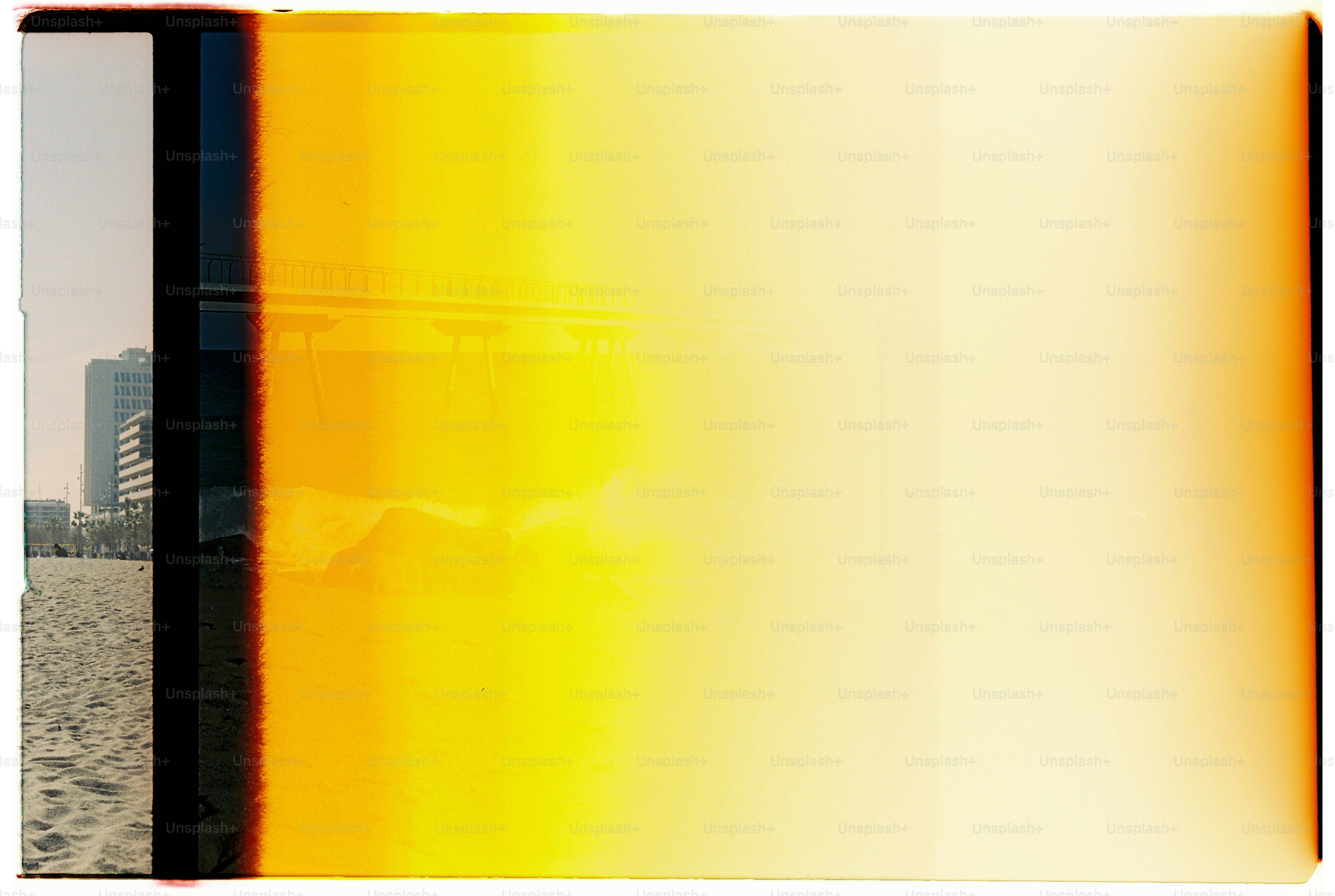A sandy beach with buildings and a bridge obscured by a bright yellow light leak.