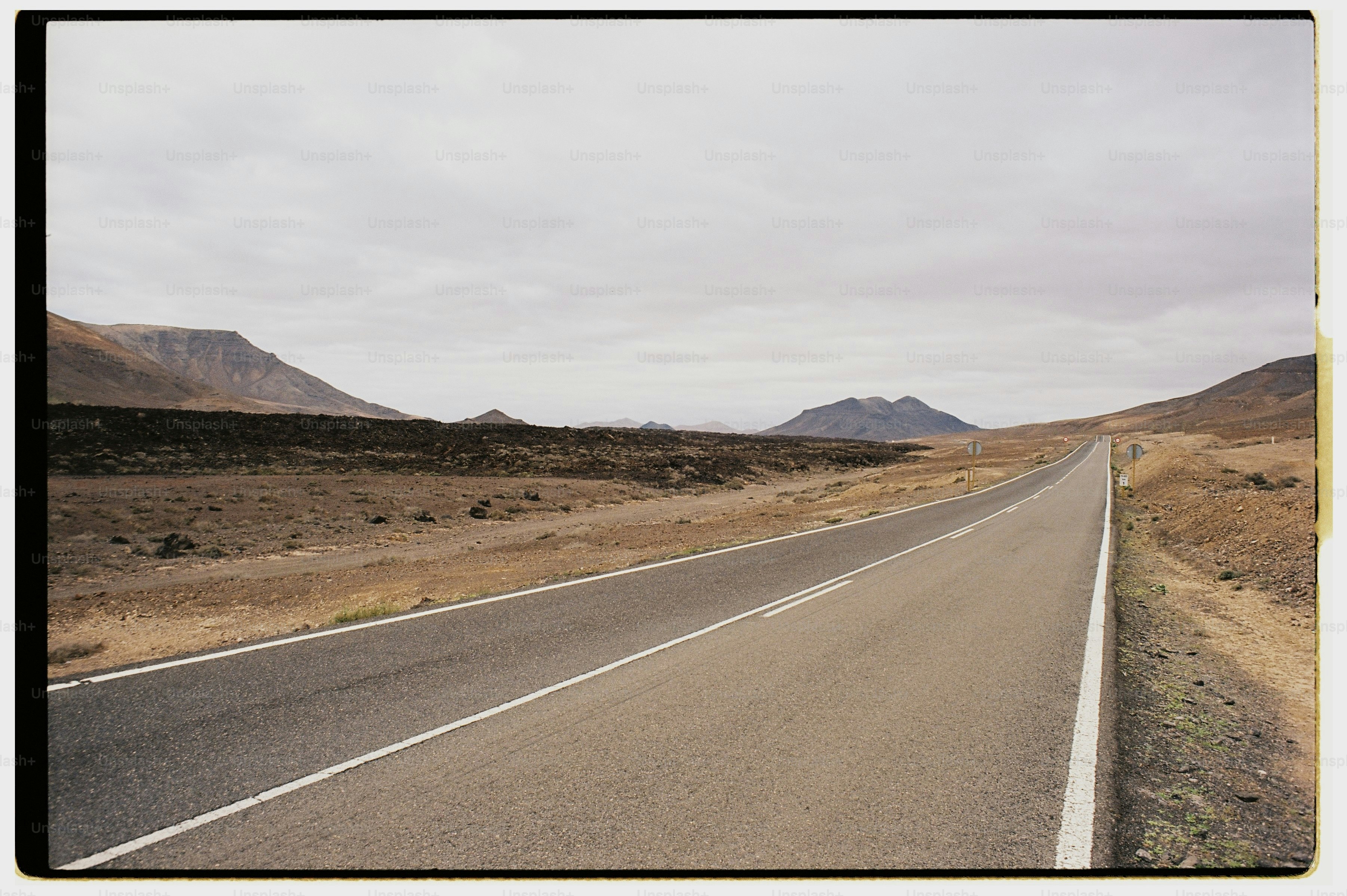 An asphalt road stretching through a barren volcanic landscape under a cloudy sky.