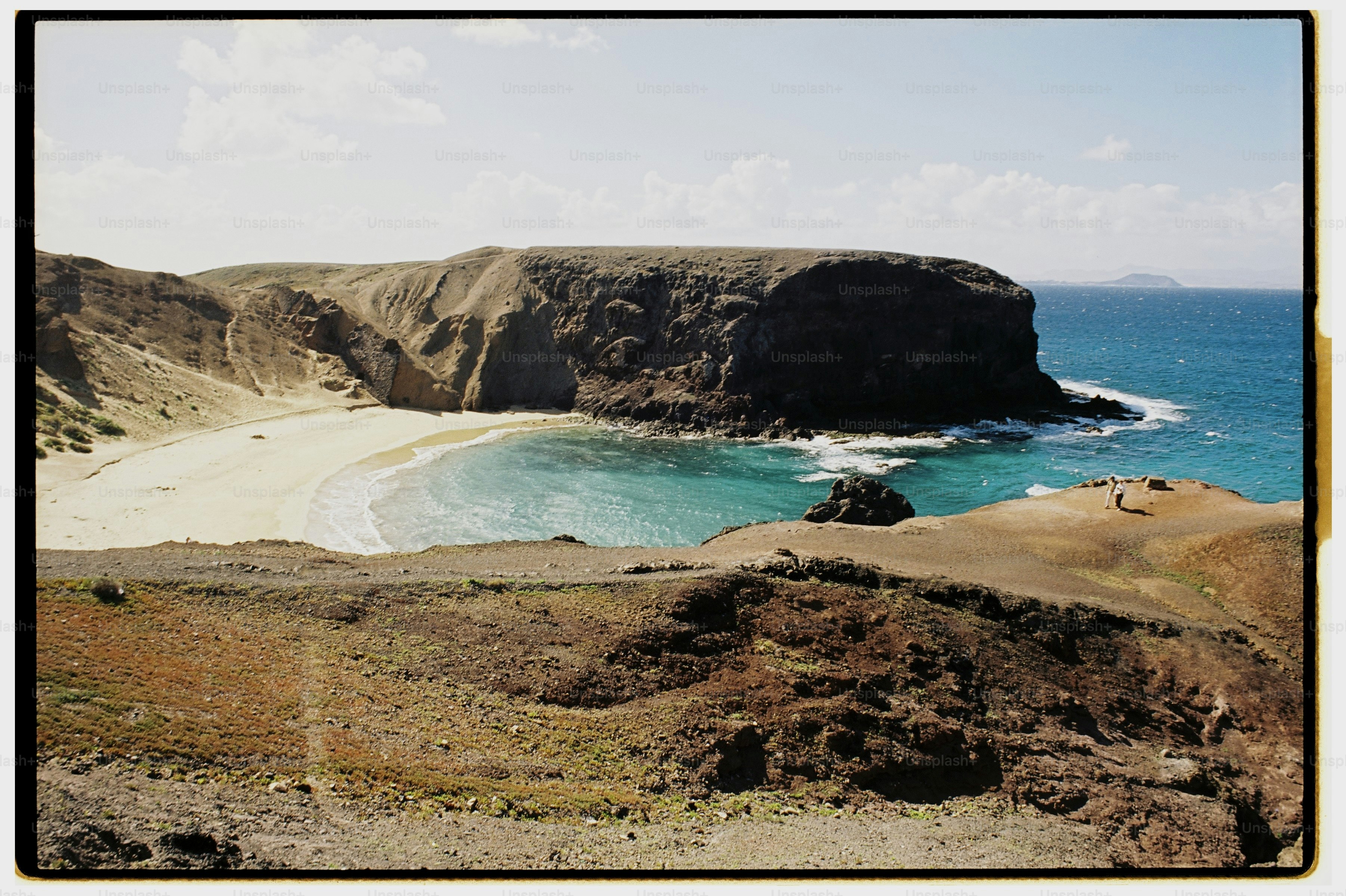A sandy beach in a cove surrounded by dark volcanic cliffs and blue water.