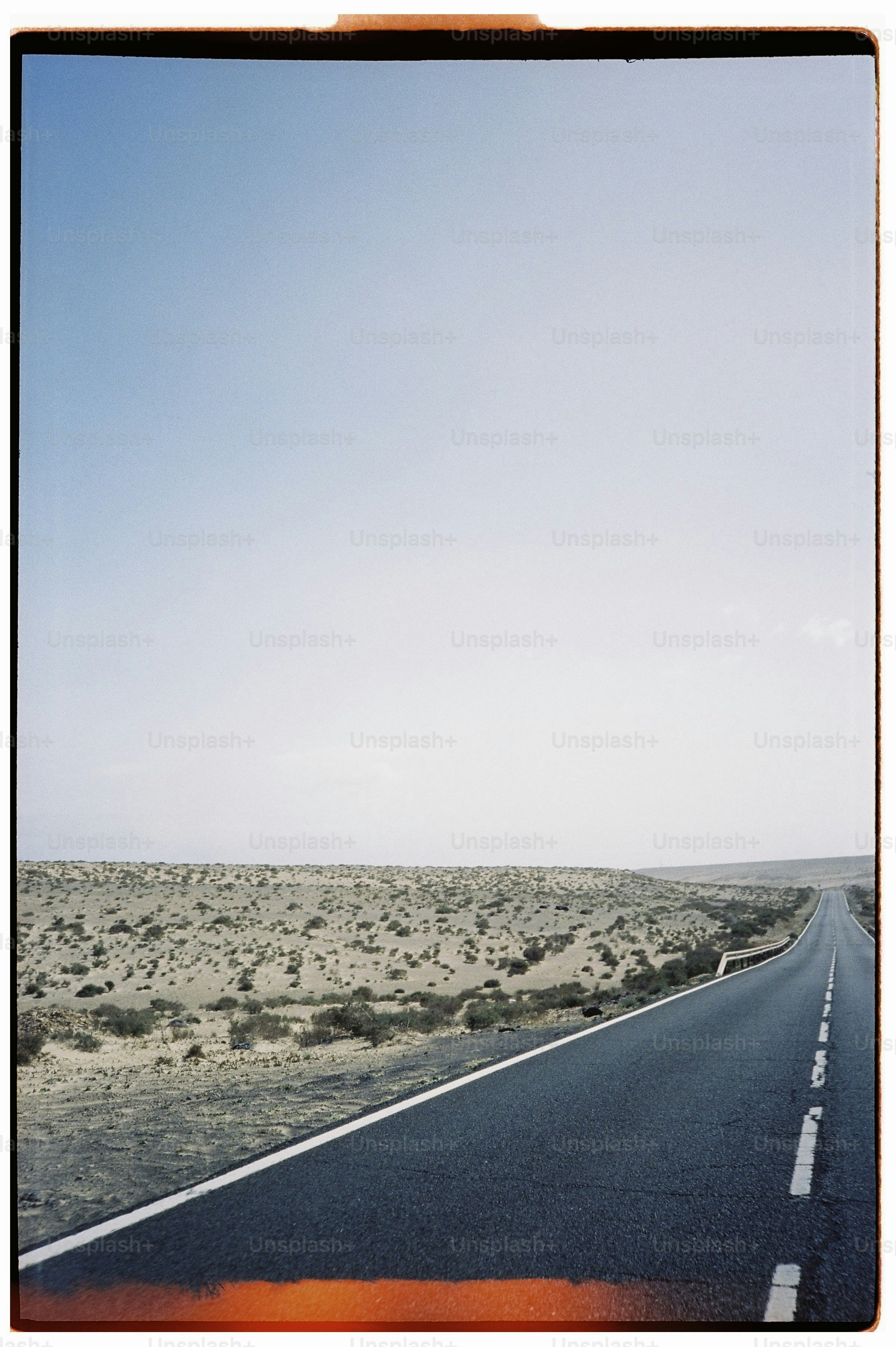 An asphalt road stretching through a vast, arid desert landscape under a clear sky.