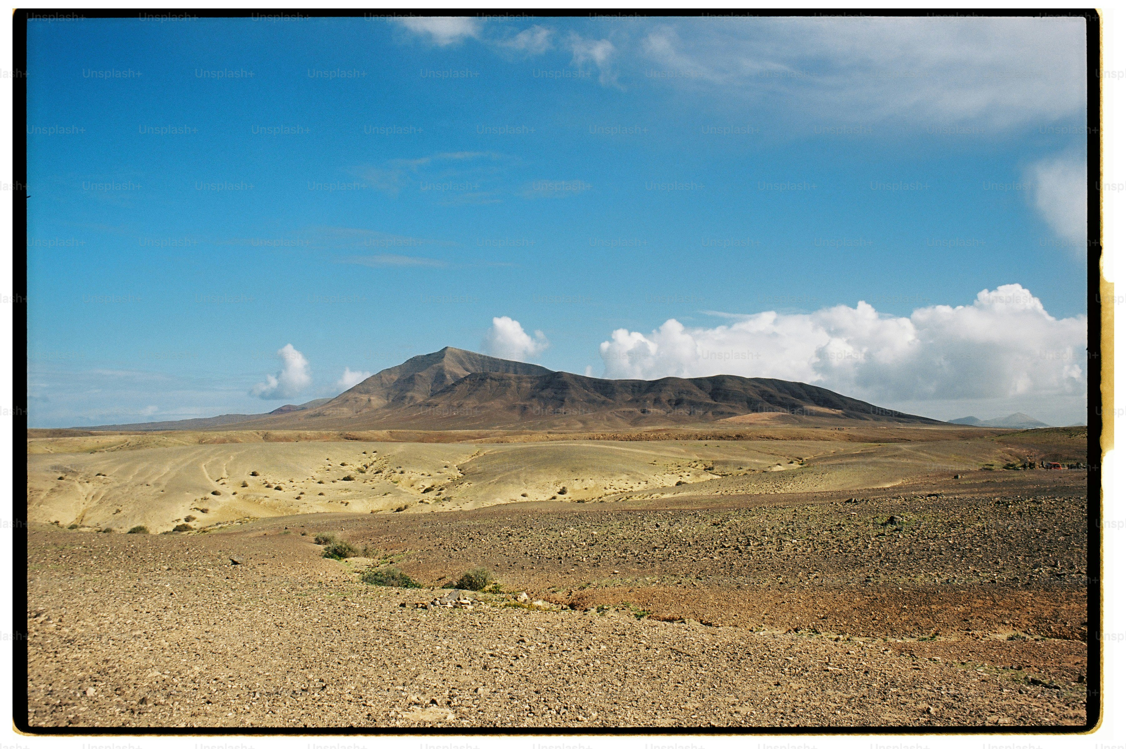 A barren volcanic landscape with a large mountain under a bright blue sky