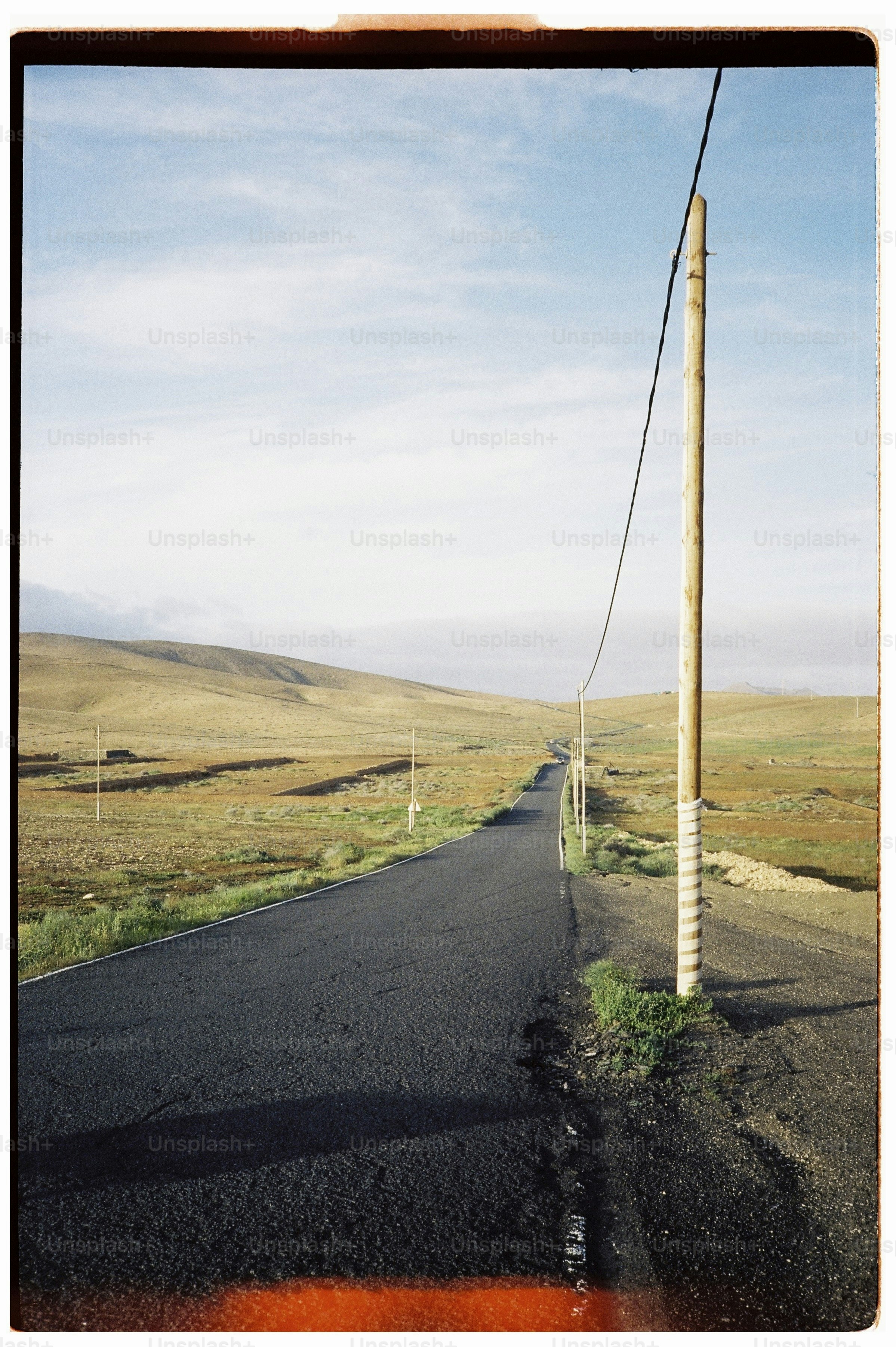 A paved road stretching through a vast, arid landscape with a wooden utility pole.