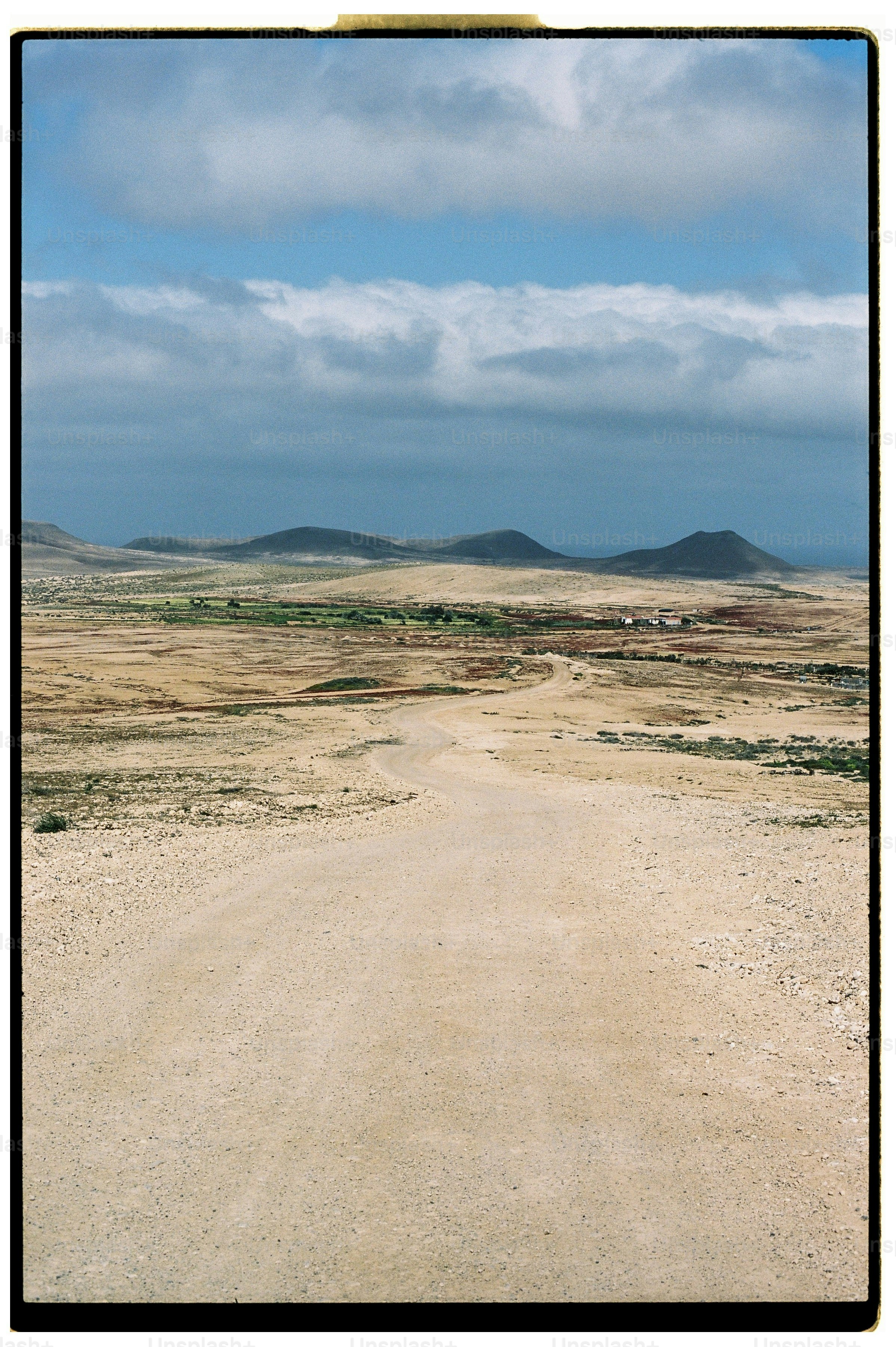 A winding dirt road through a vast arid landscape under a cloudy sky.