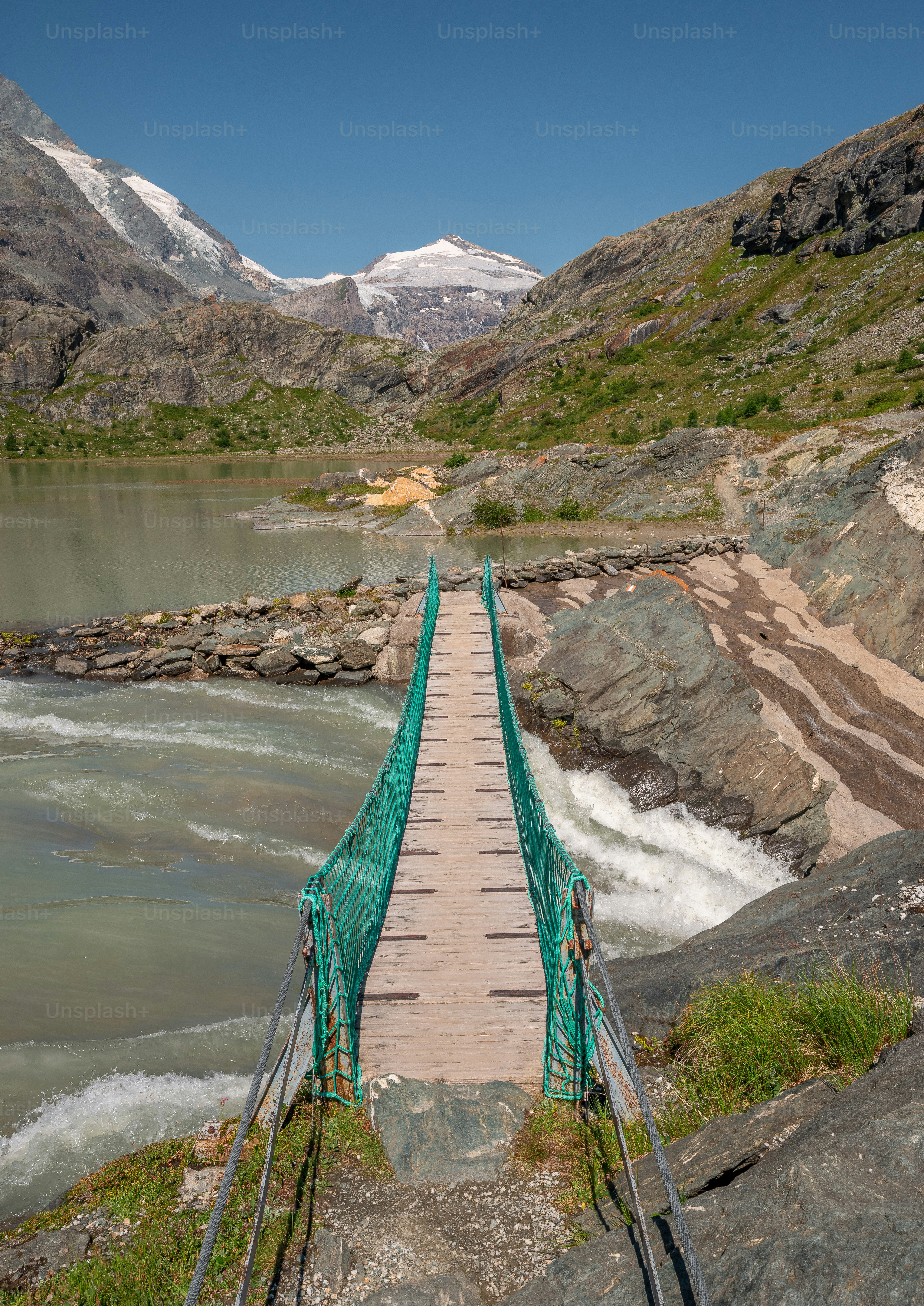 A wooden footbridge with green netting over a stream in the Hohe Tauern mountains