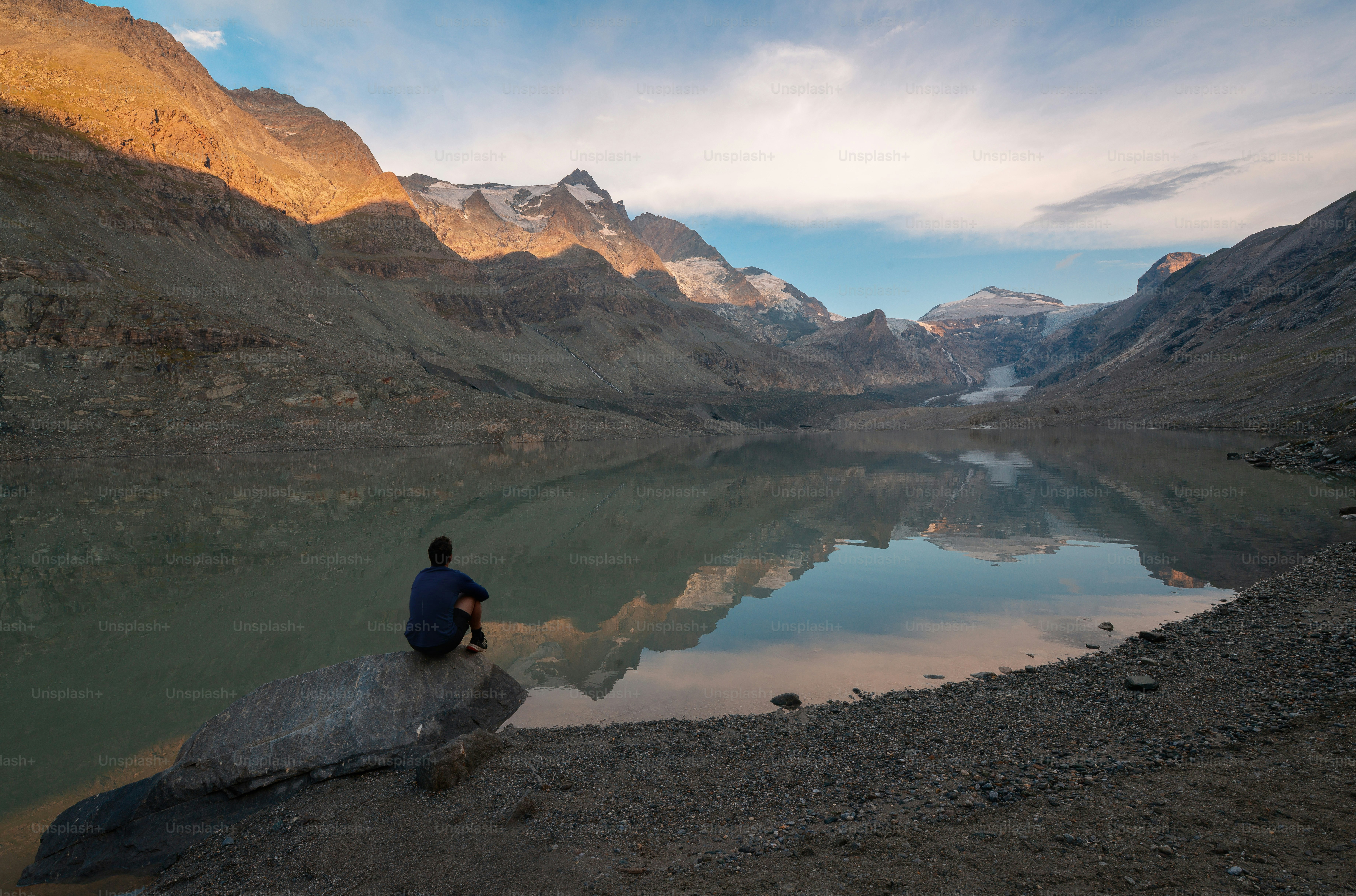 A person on a rock overlooking a lake reflecting mountains in Hohe Tauern