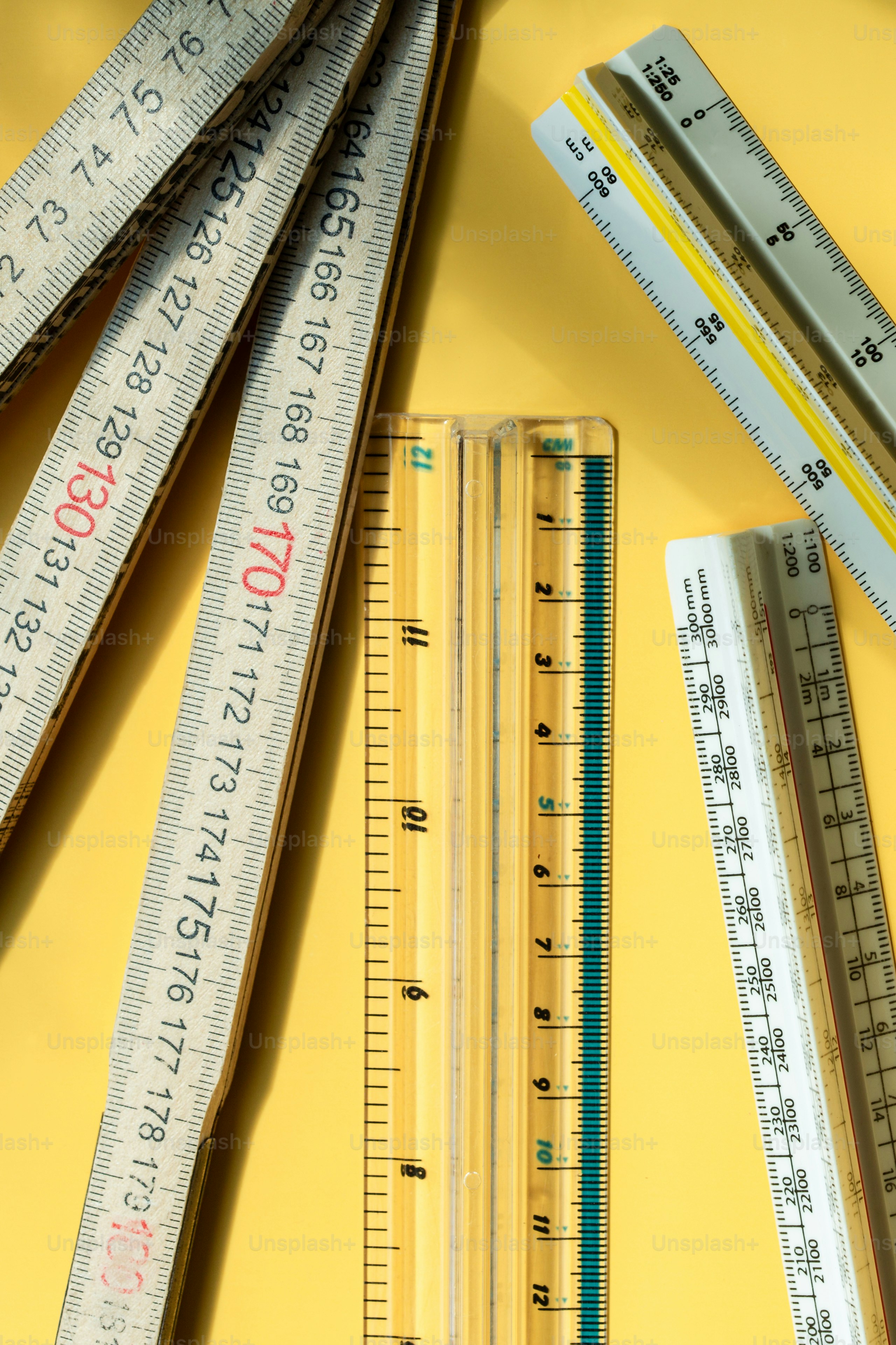 A collection of wooden folding rulers and plastic architectural scales on a yellow surface.