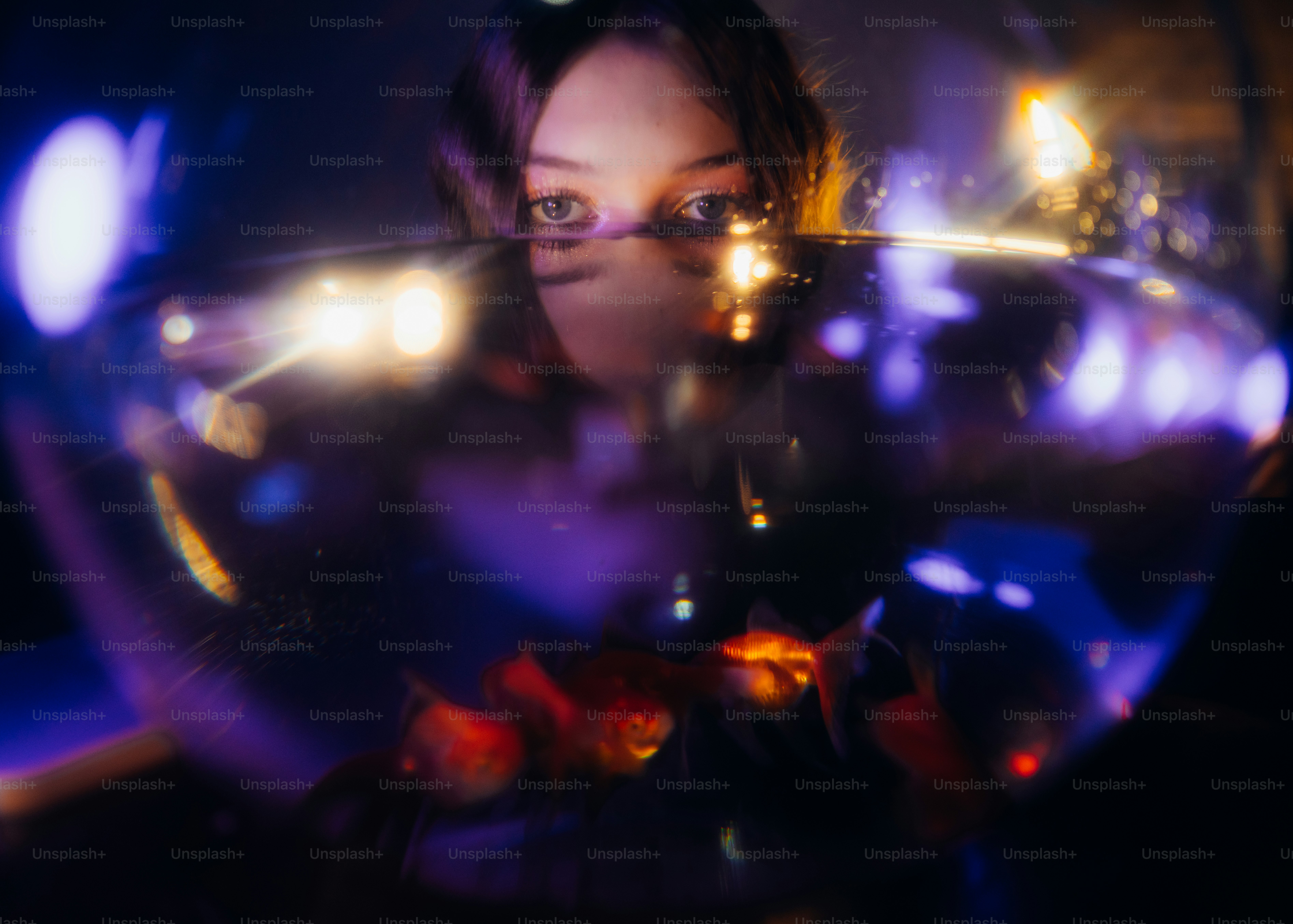 A person looking through a glass bowl containing goldfish in dim purple light