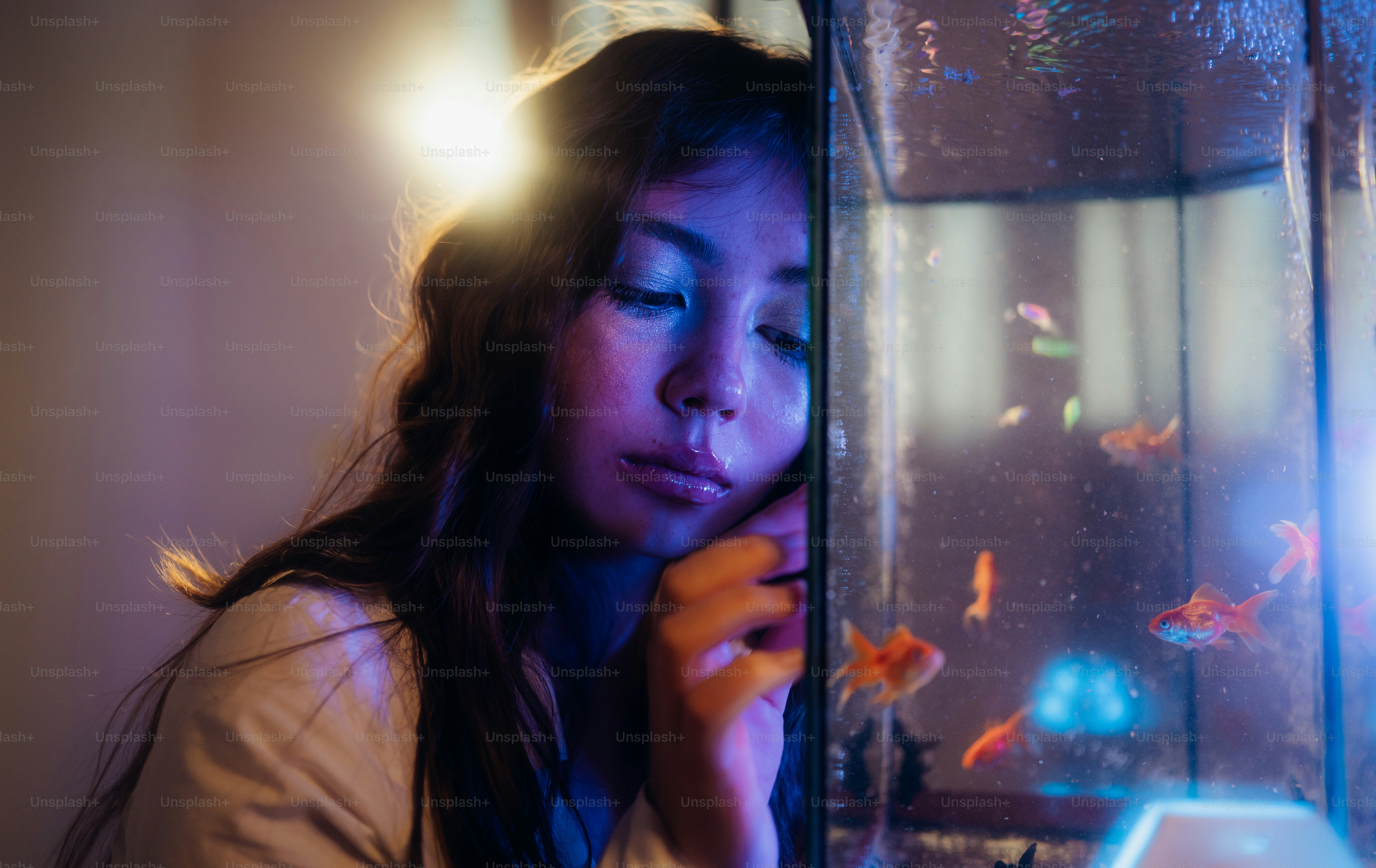 Woman with closed eyes leaning on illuminated goldfish aquarium