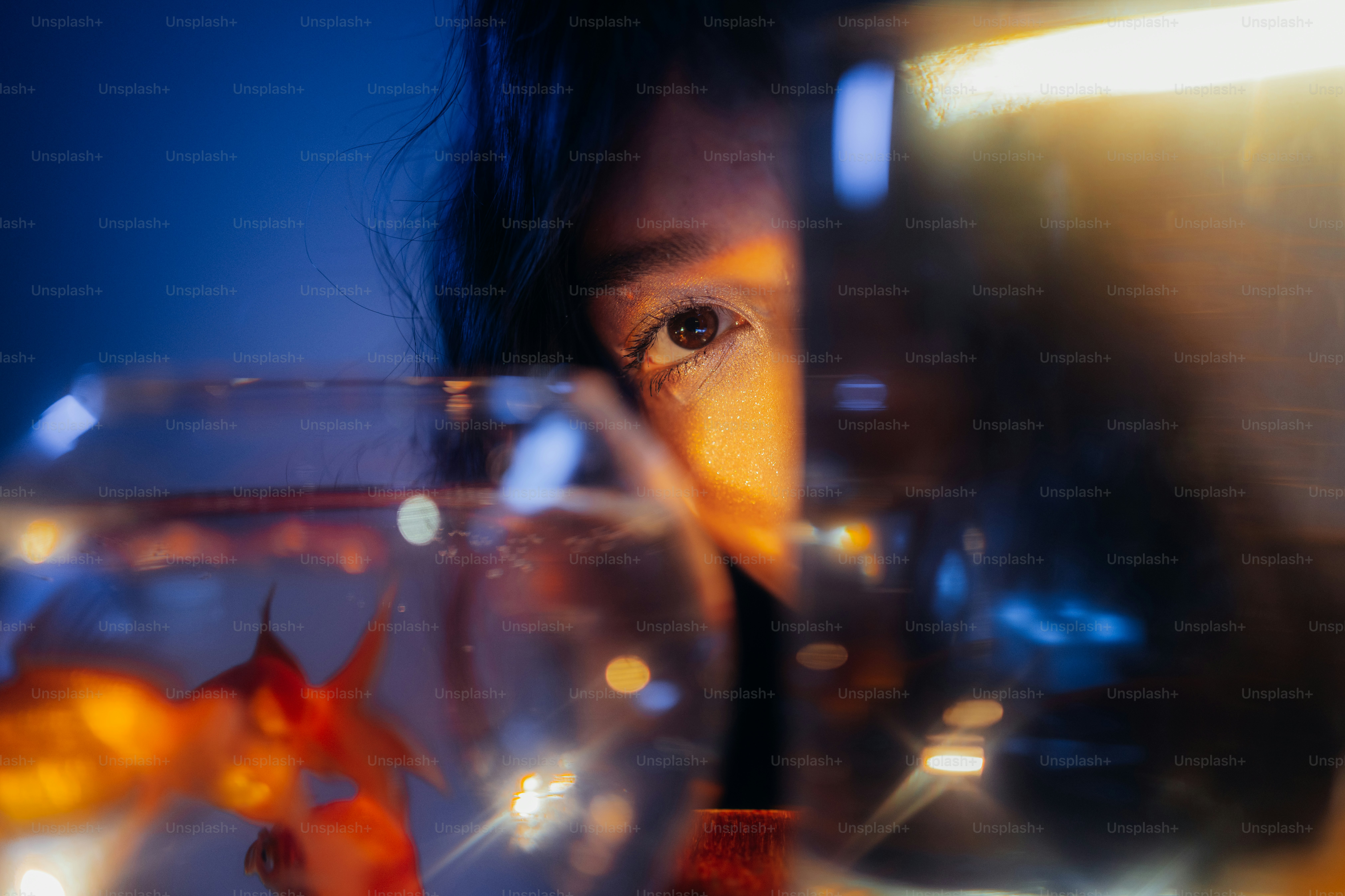 Eye looking through glass with goldfish and glowing bokeh
