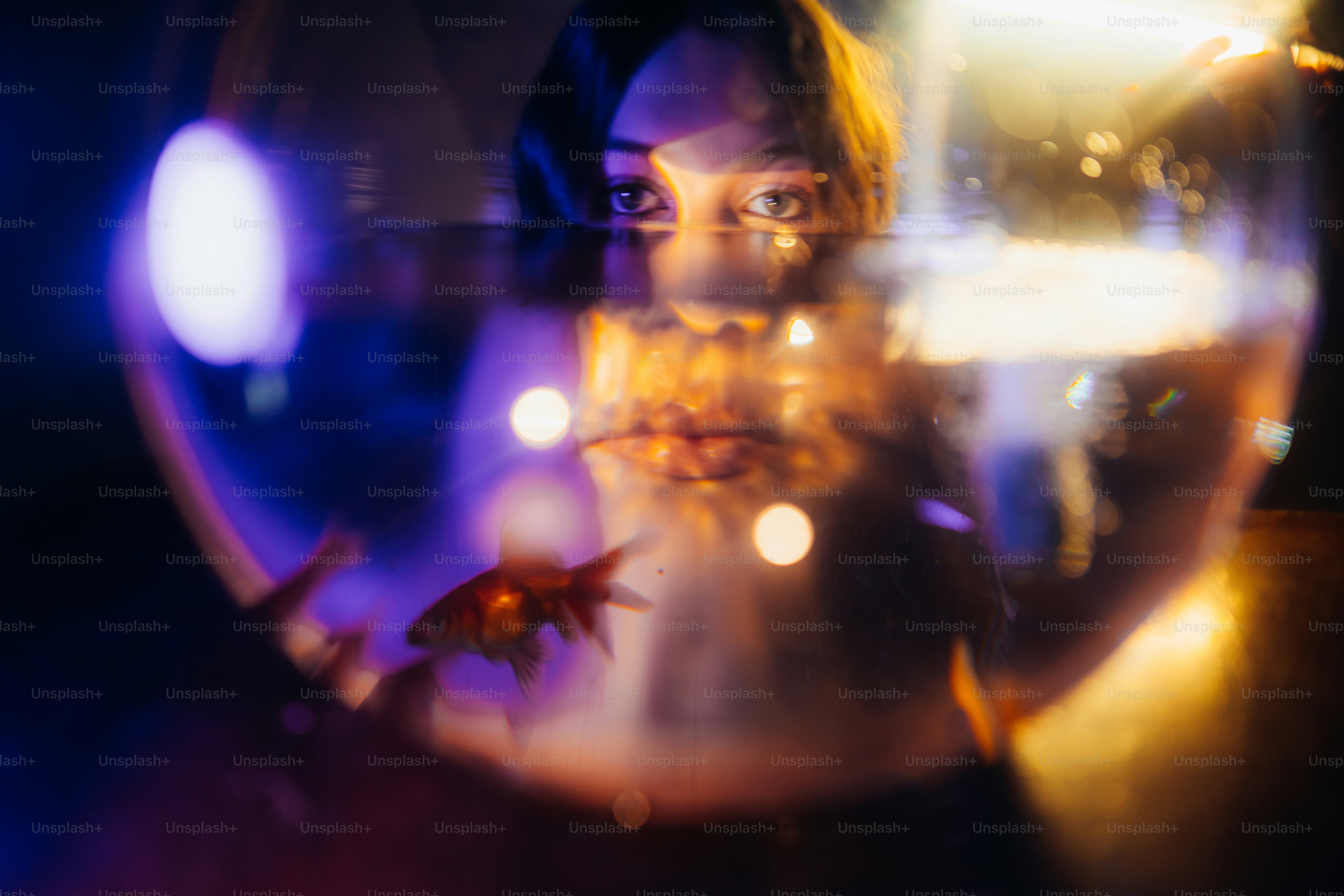 Woman's eyes reflected in glowing fishbowl with goldfish