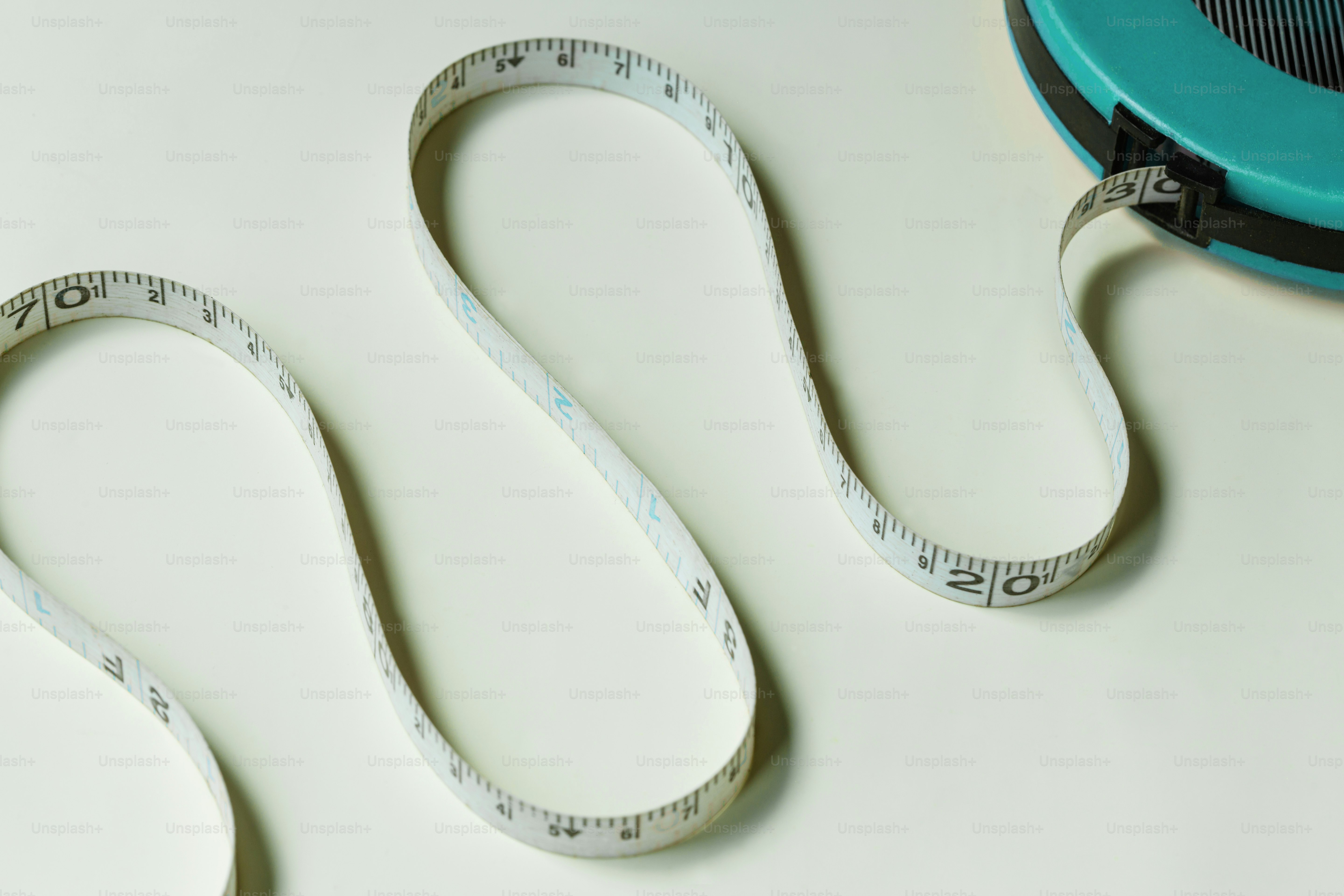 A white measuring tape extending from a teal plastic case on a light surface.