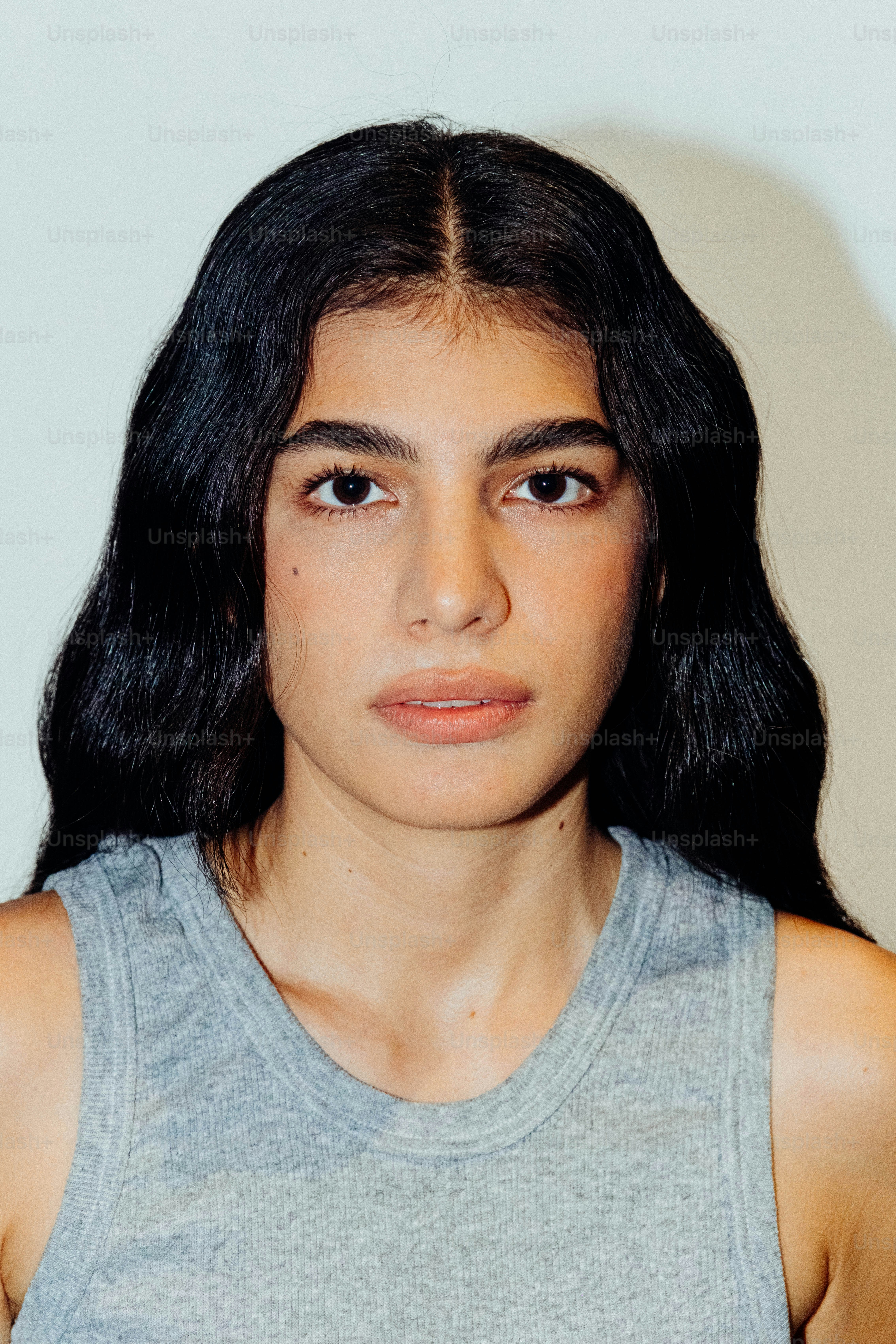 A woman with long dark hair wearing a grey ribbed tank top