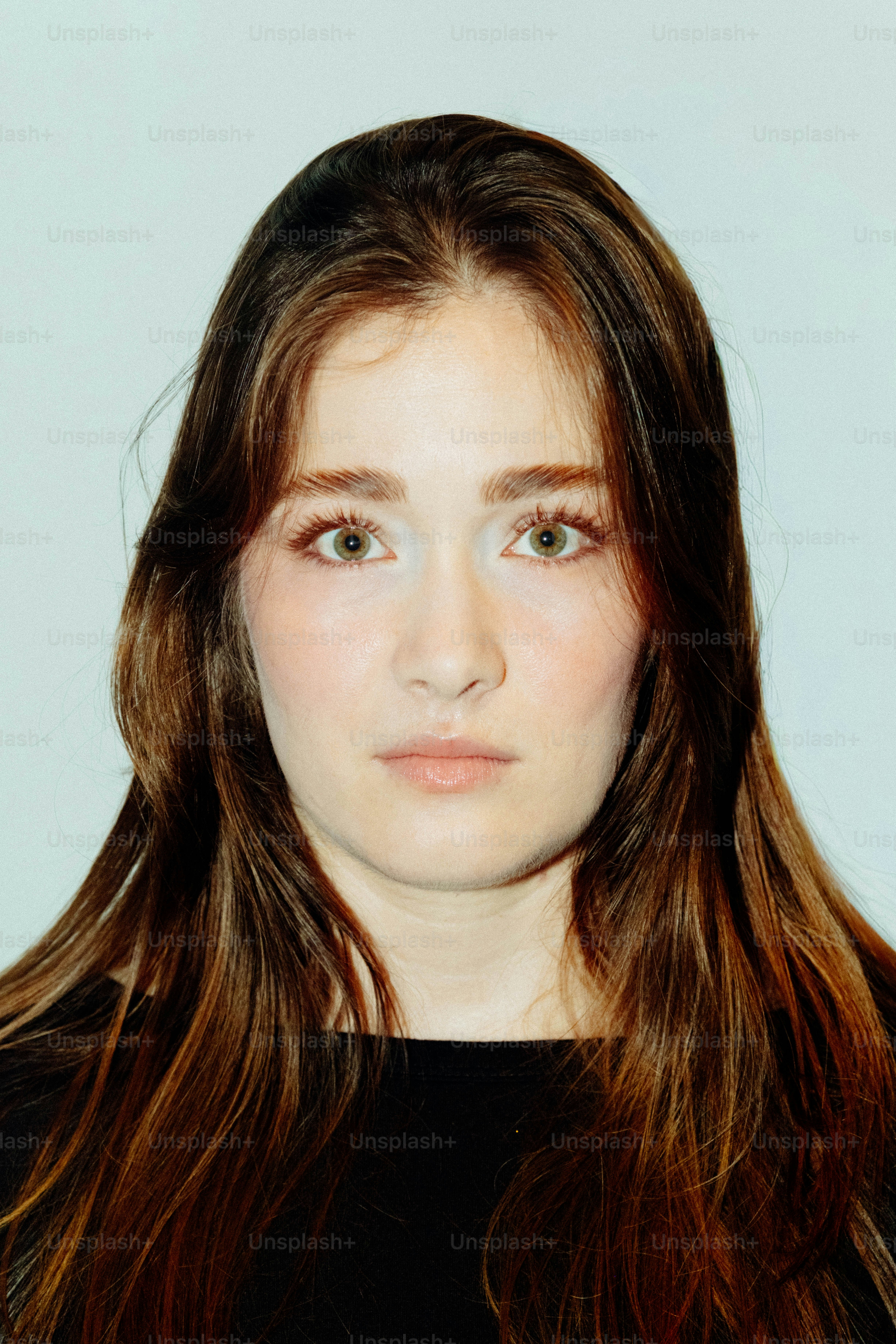 A woman with long brown hair and green eyes against a plain background