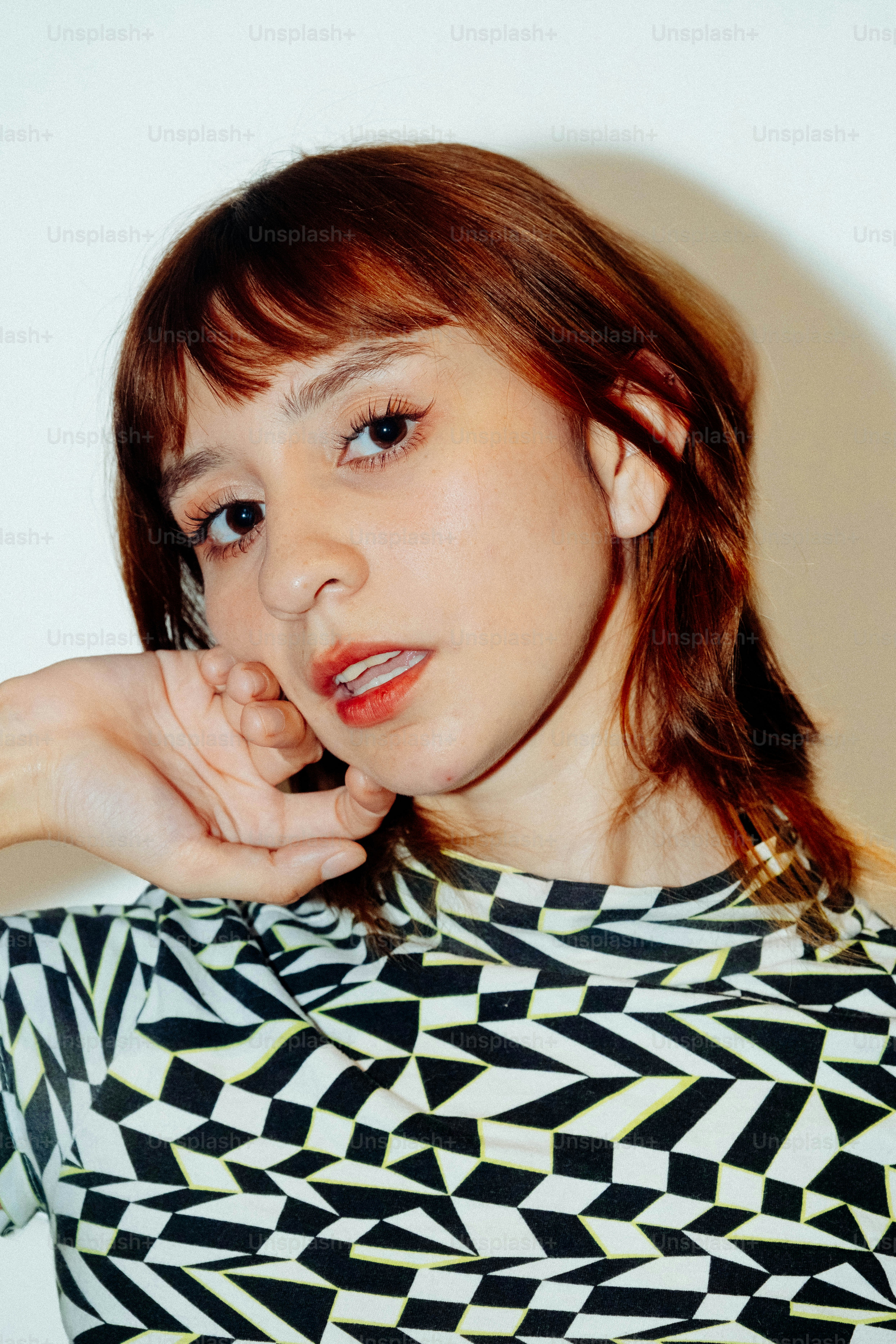 A woman with auburn hair wearing a black and white geometric patterned shirt