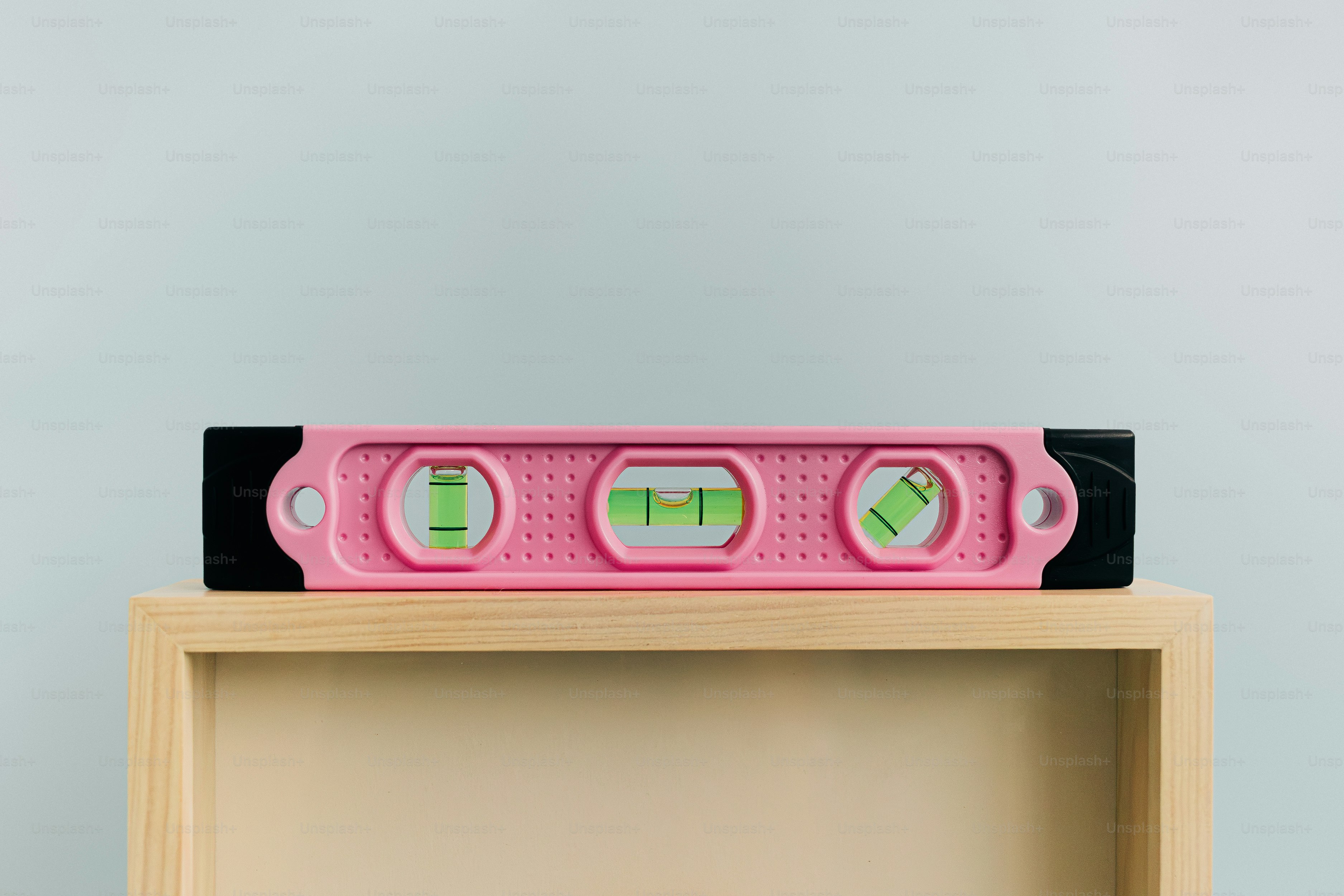 A pink spirit level with three vials on a light wooden surface.