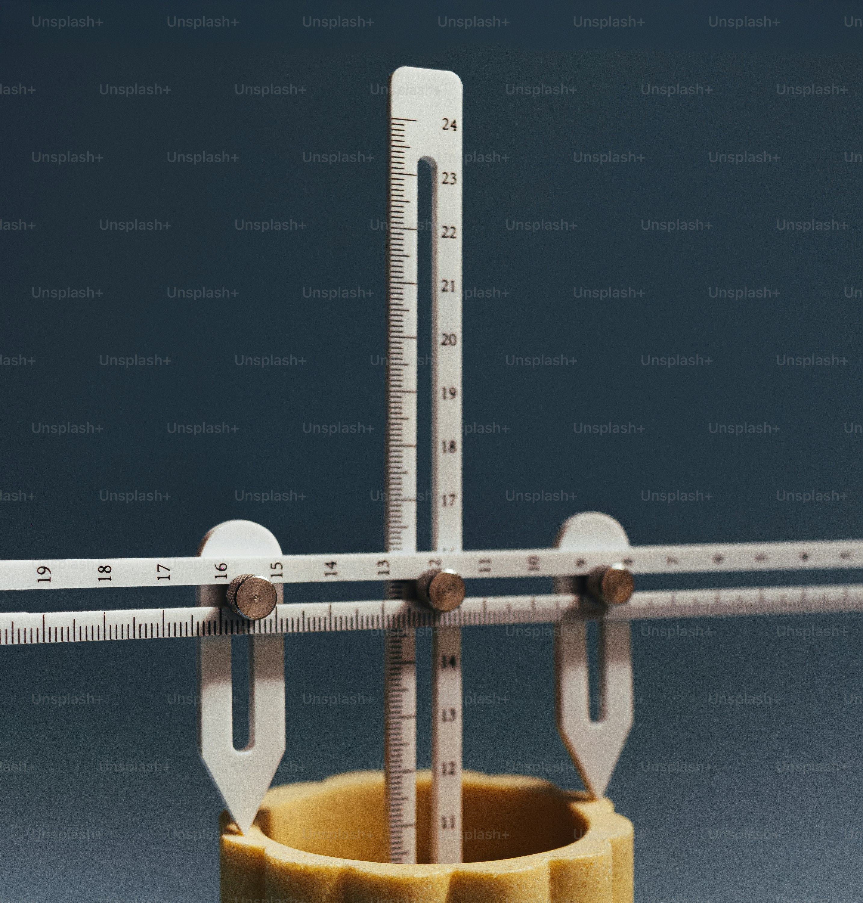 A white plastic measuring tool with metal screws on a yellow cylindrical object.