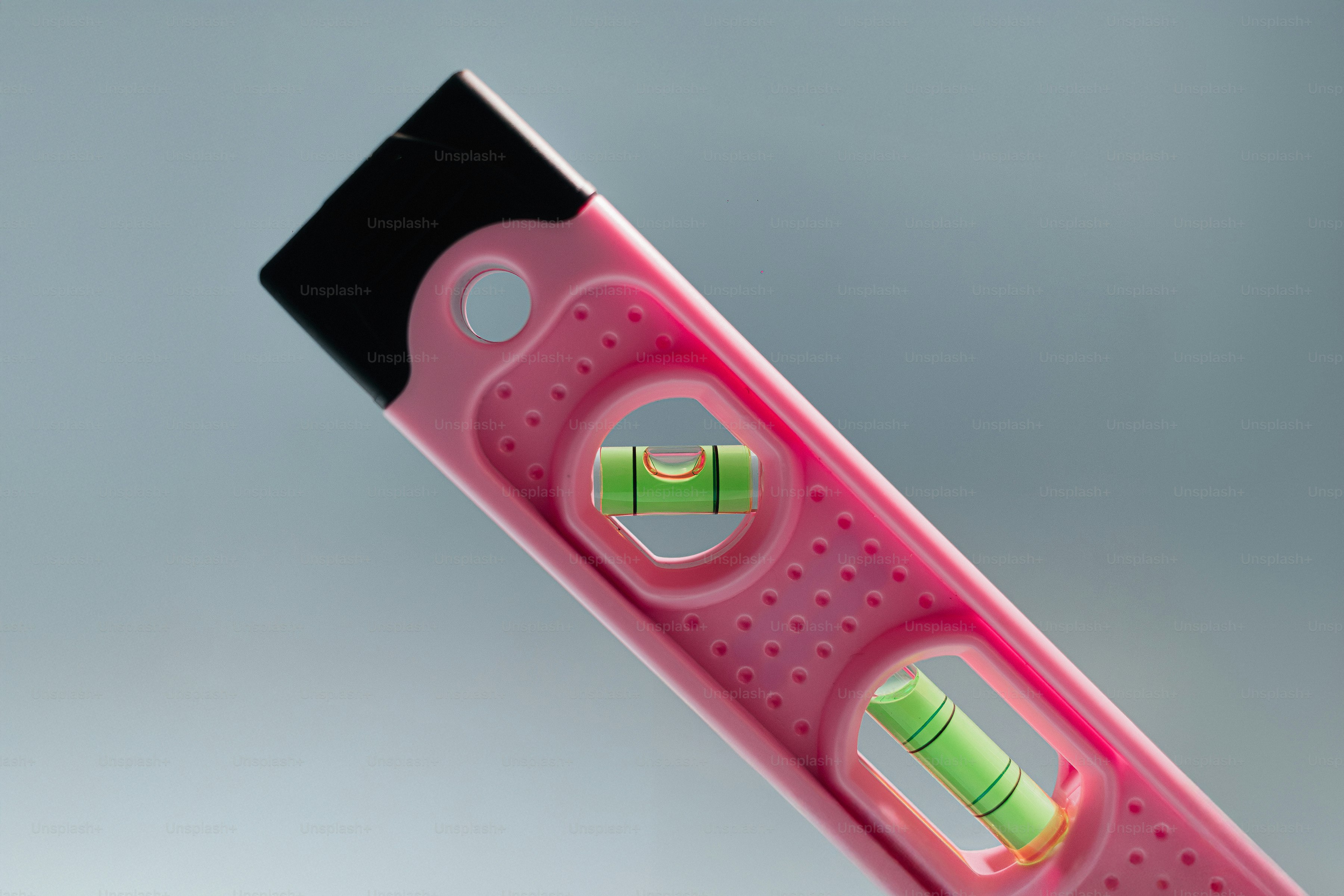 A pink spirit level with two green liquid vials against a grey background.