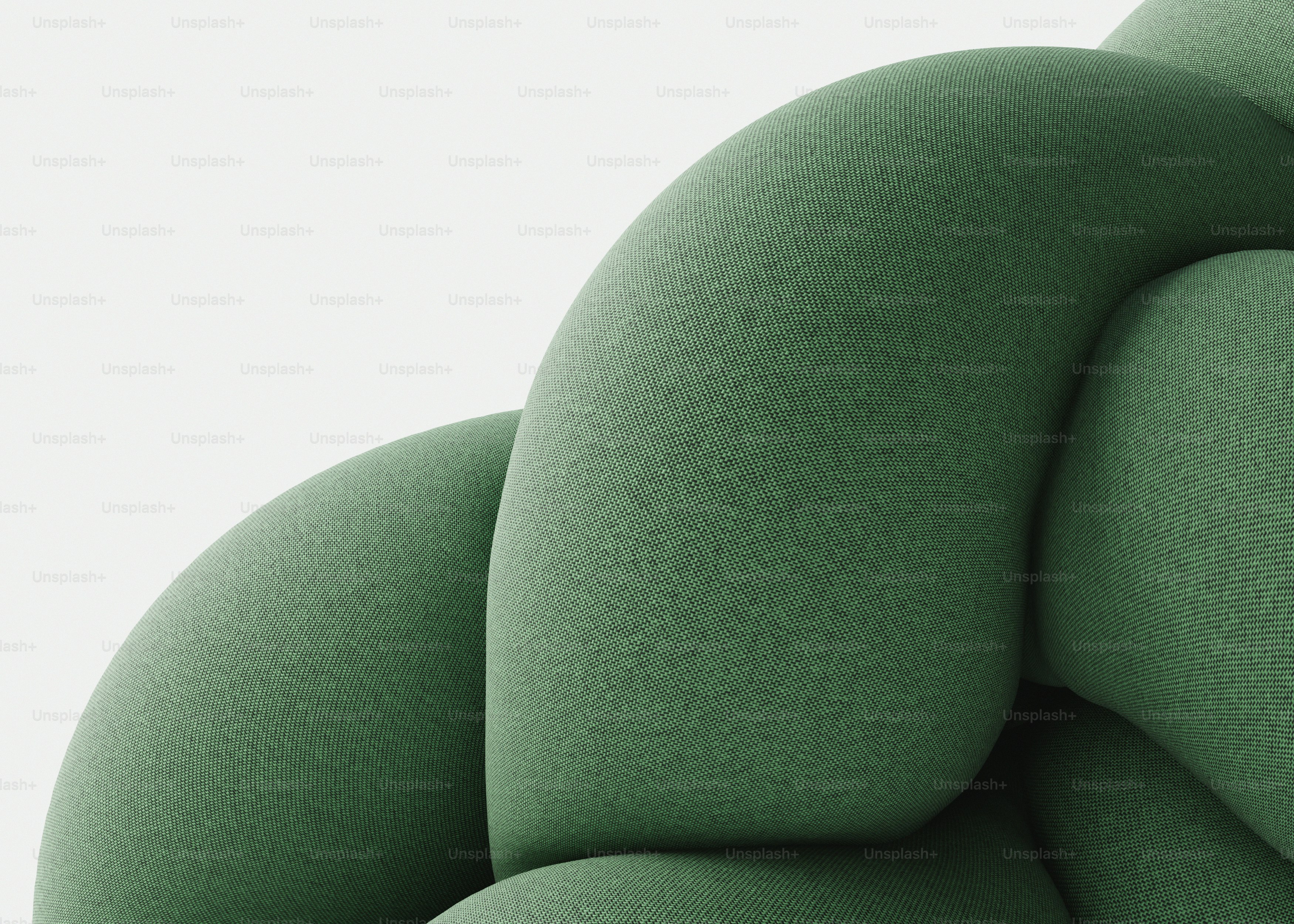 A close-up of a green fabric knot pillow against a white background