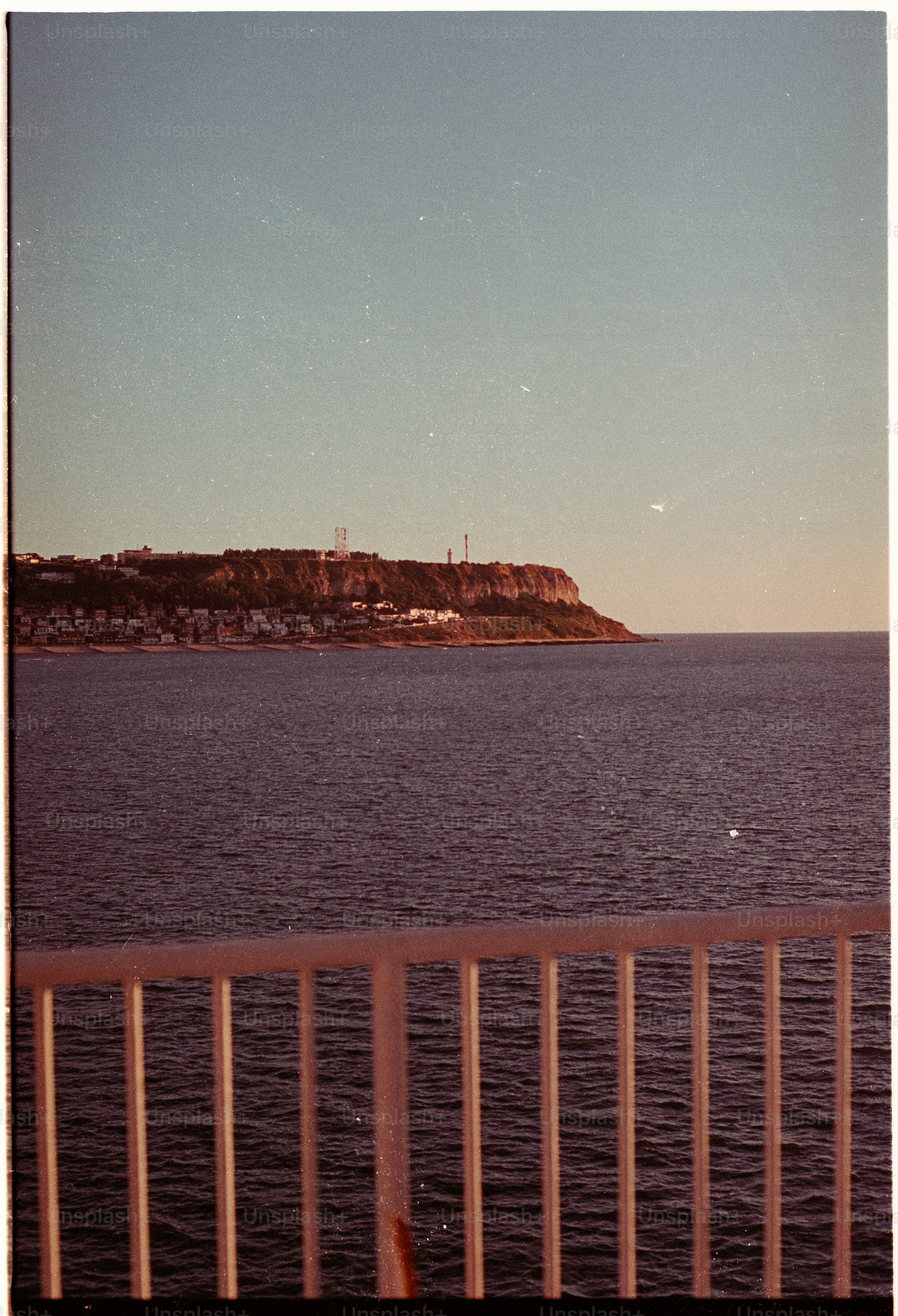 A coastal cliff with buildings above the sea, viewed past a white railing
