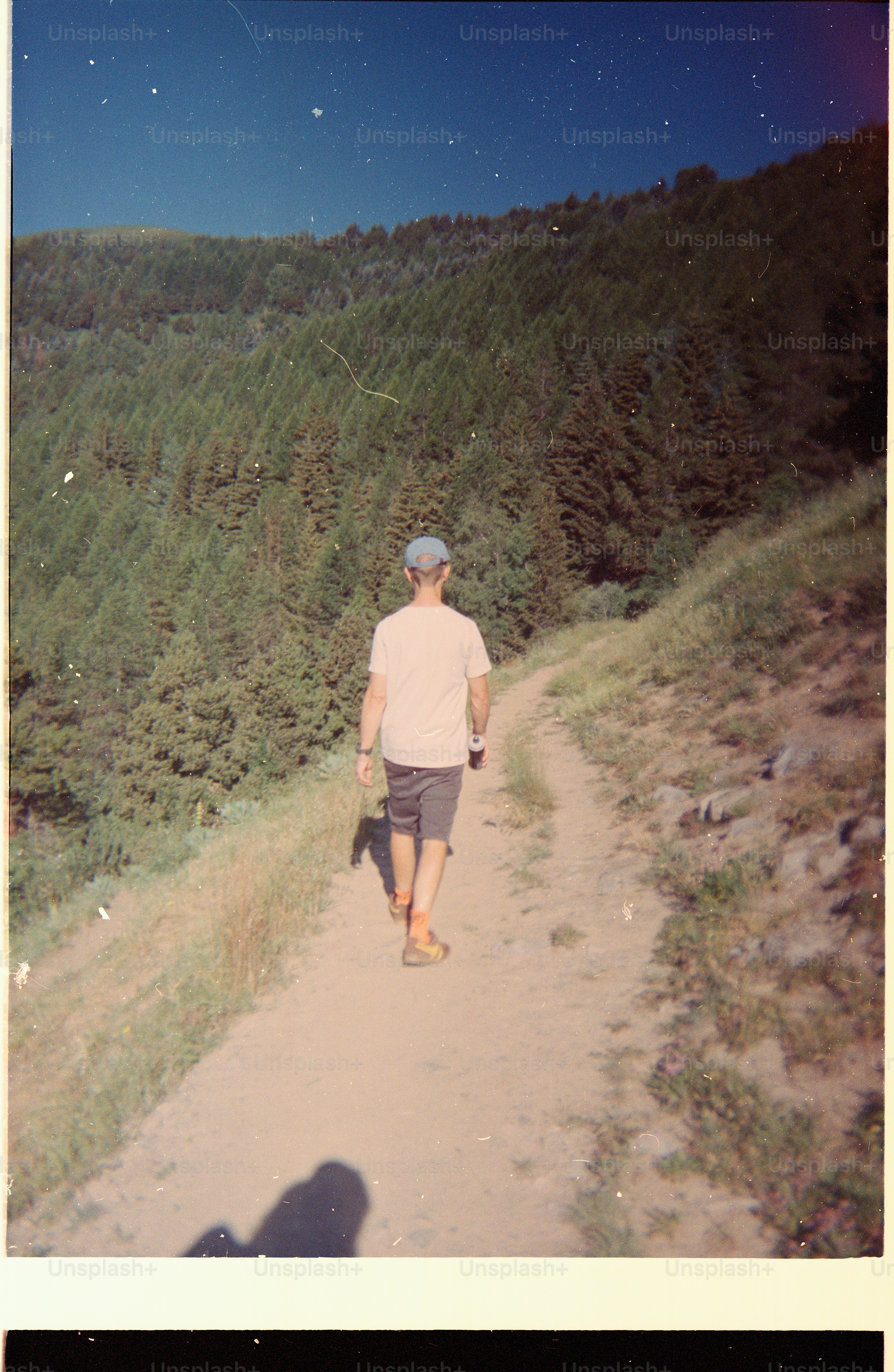 A person in a cap and t-shirt walking along a dirt trail.