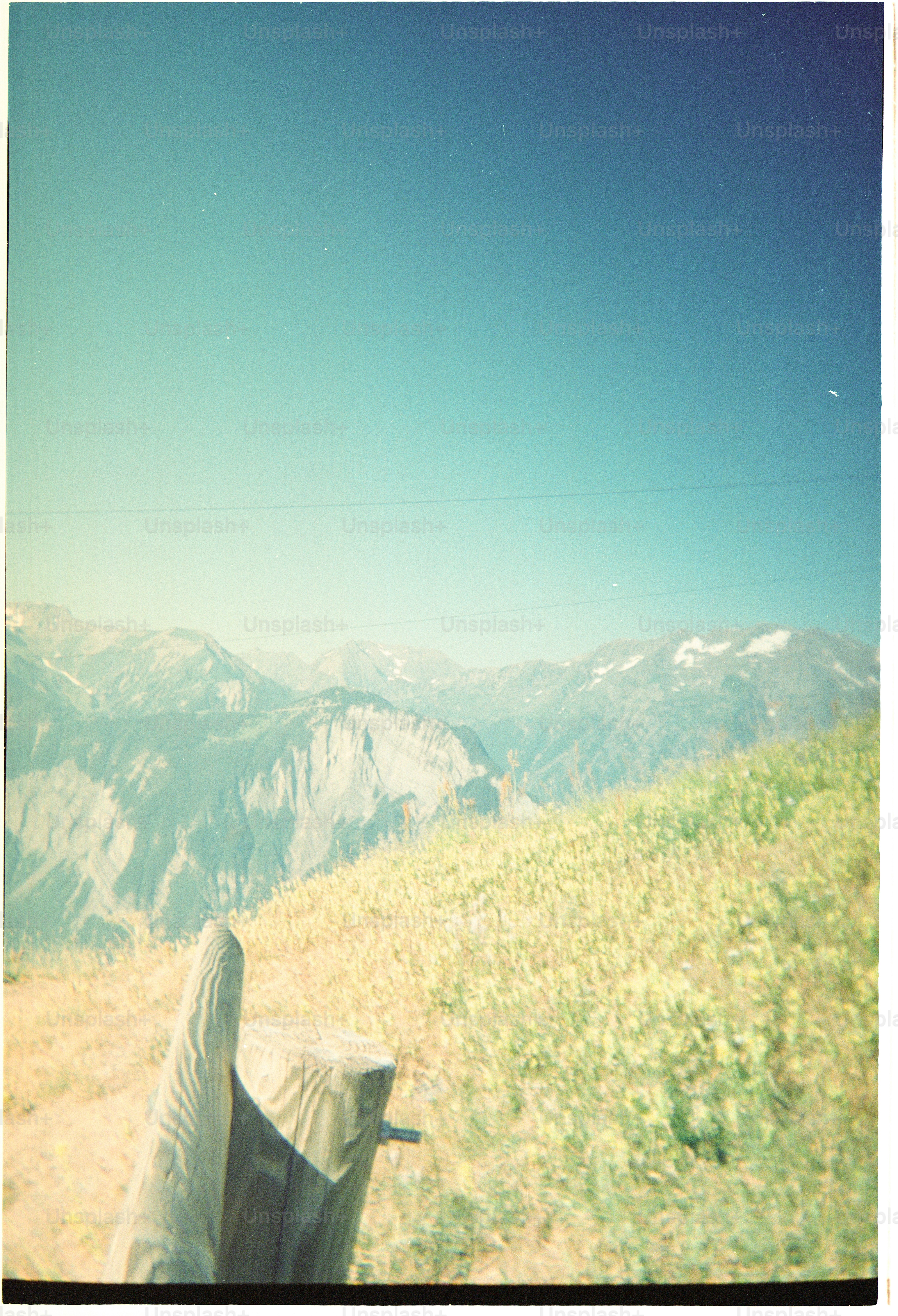 A wooden post in a grassy mountain meadow with distant peaks under a clear sky