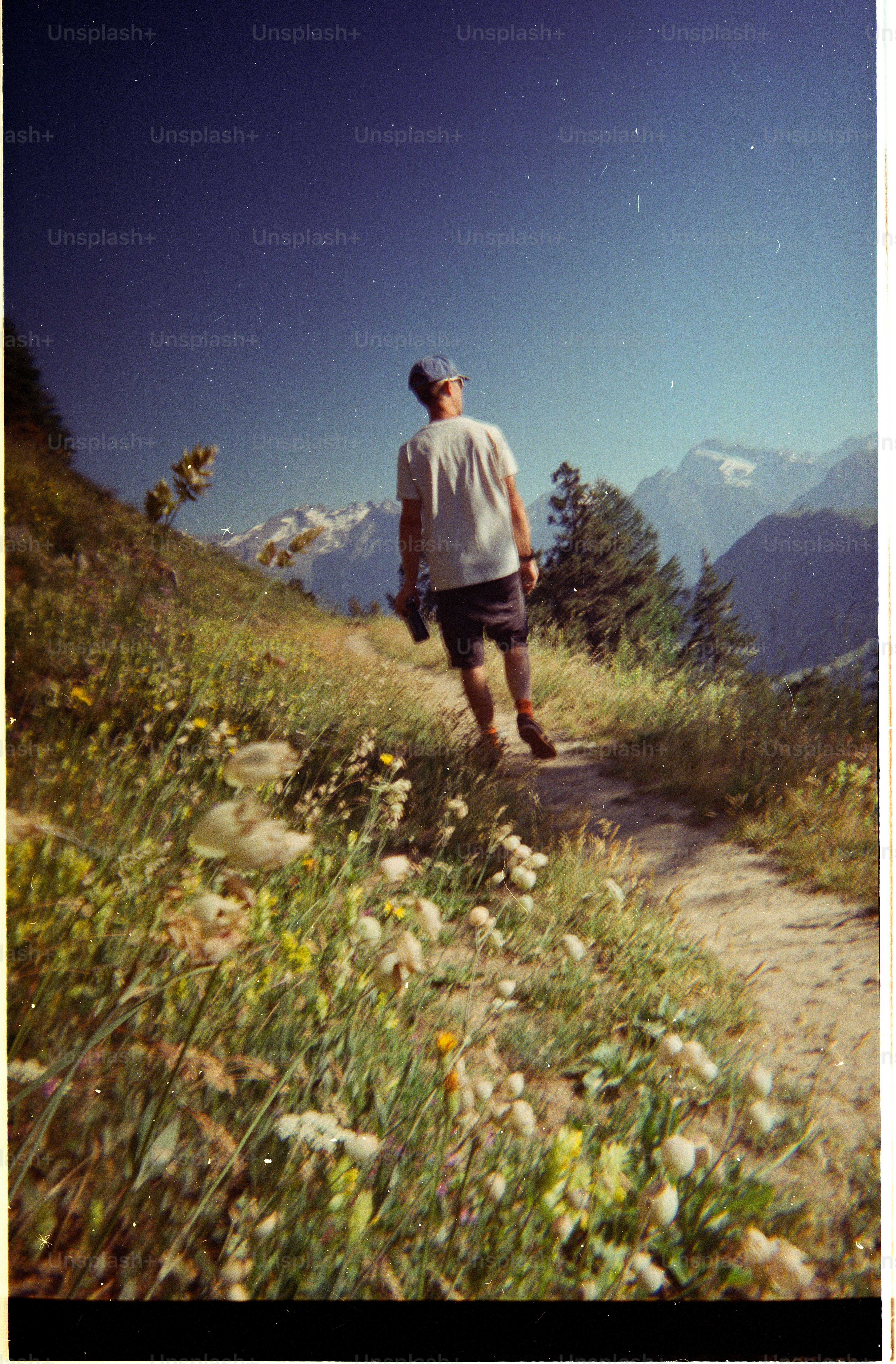 A person in a cap and t-shirt walking along a mountain trail.