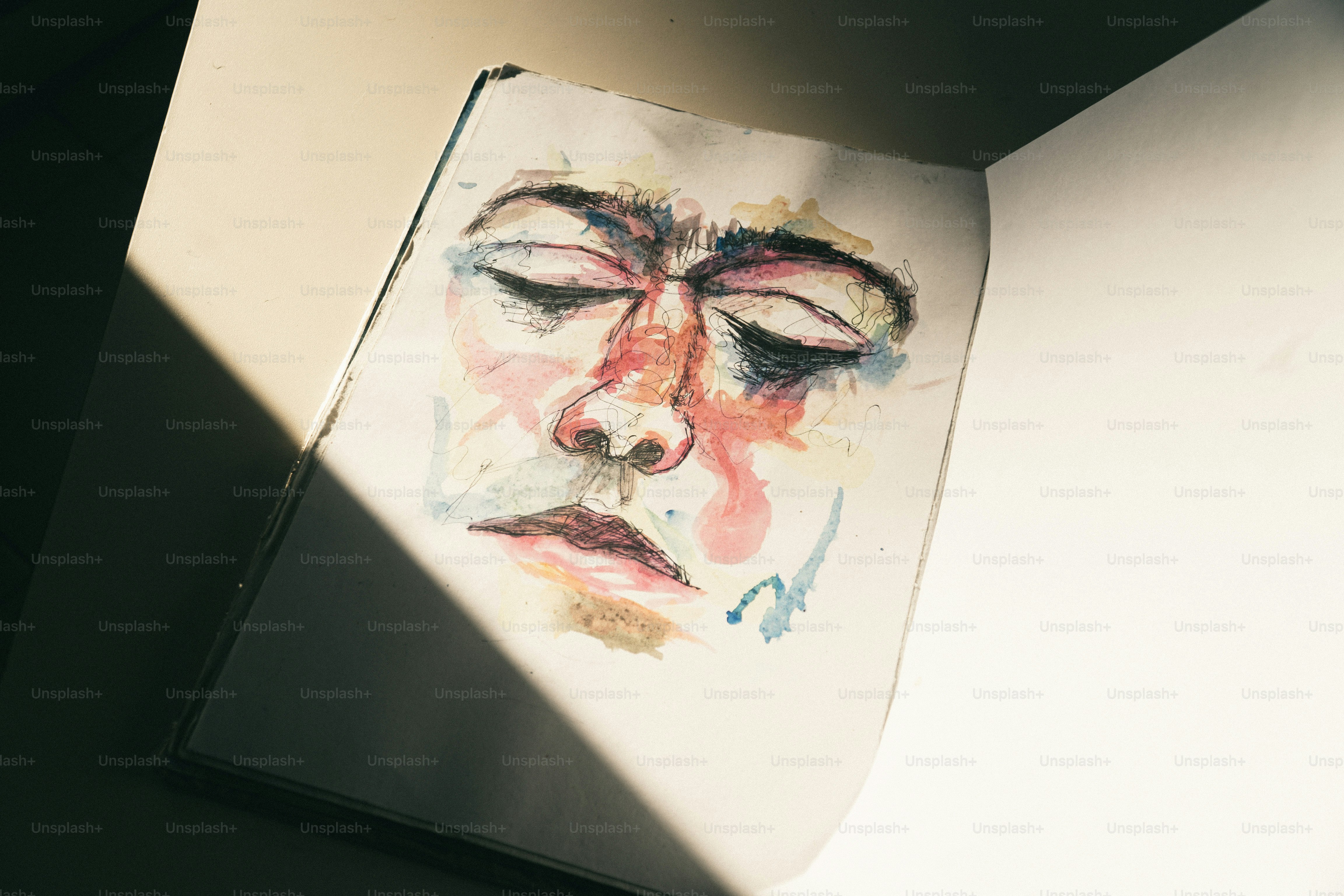A watercolor sketch of a face with closed eyes in an open sketchbook.