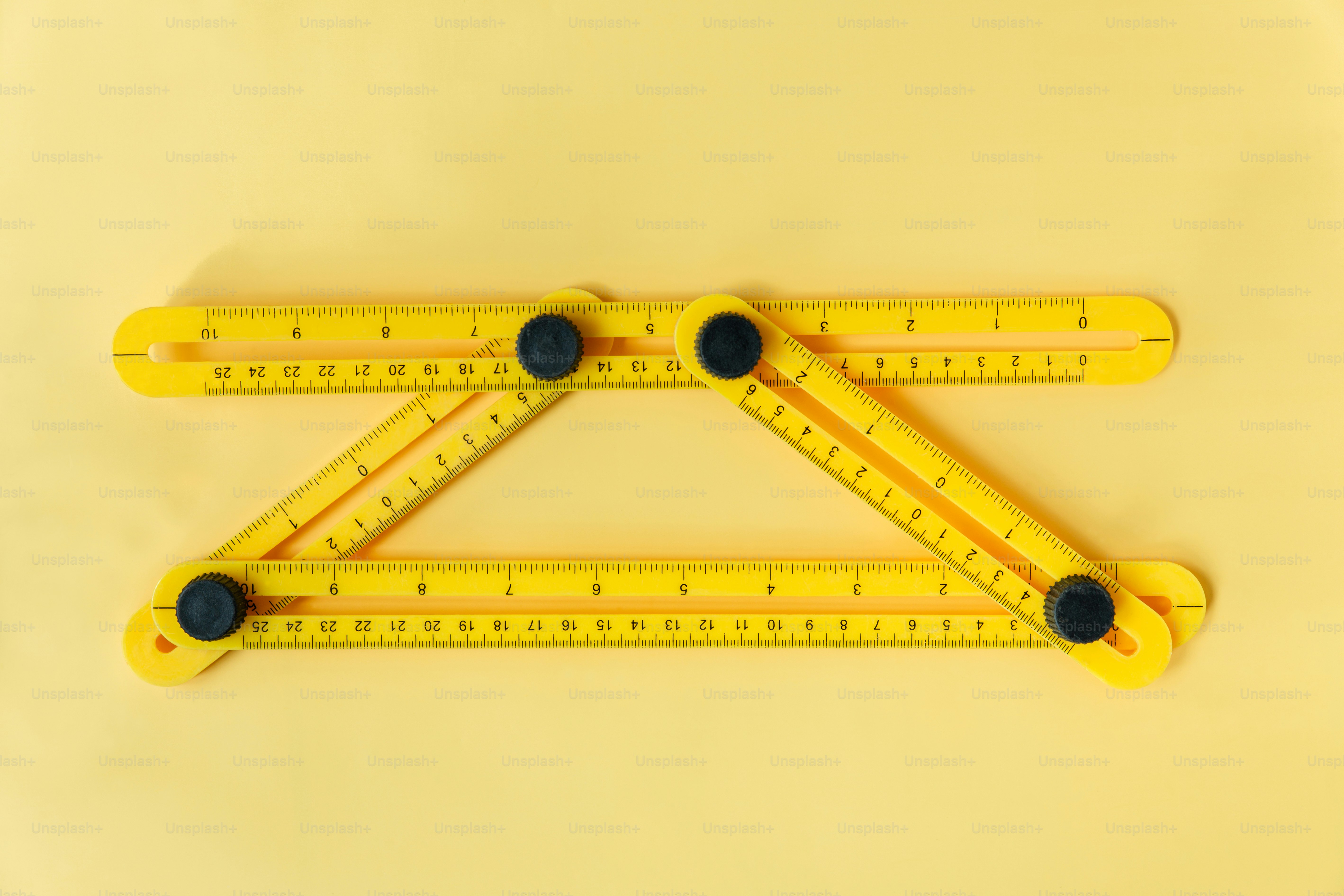 A yellow multi-angle measuring tool with black knobs on a yellow background.