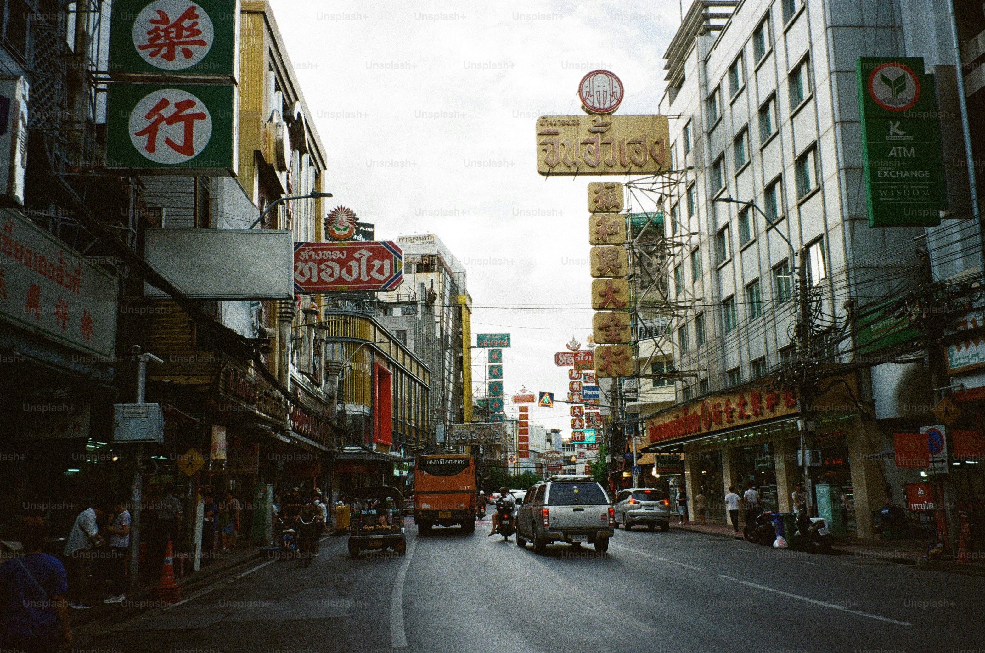 A busy street in Bangkok with cars, a bus, and many hanging neon signs