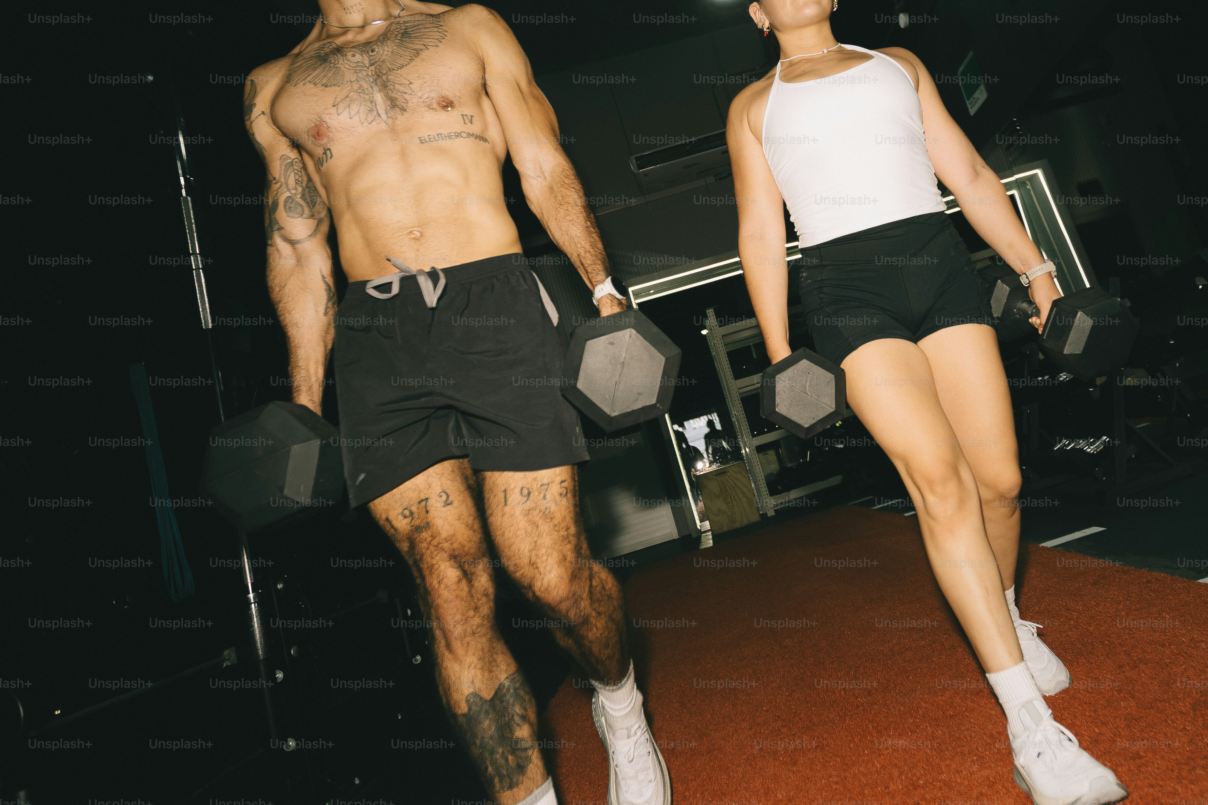 A man and a woman walking with dumbbells in a gym.